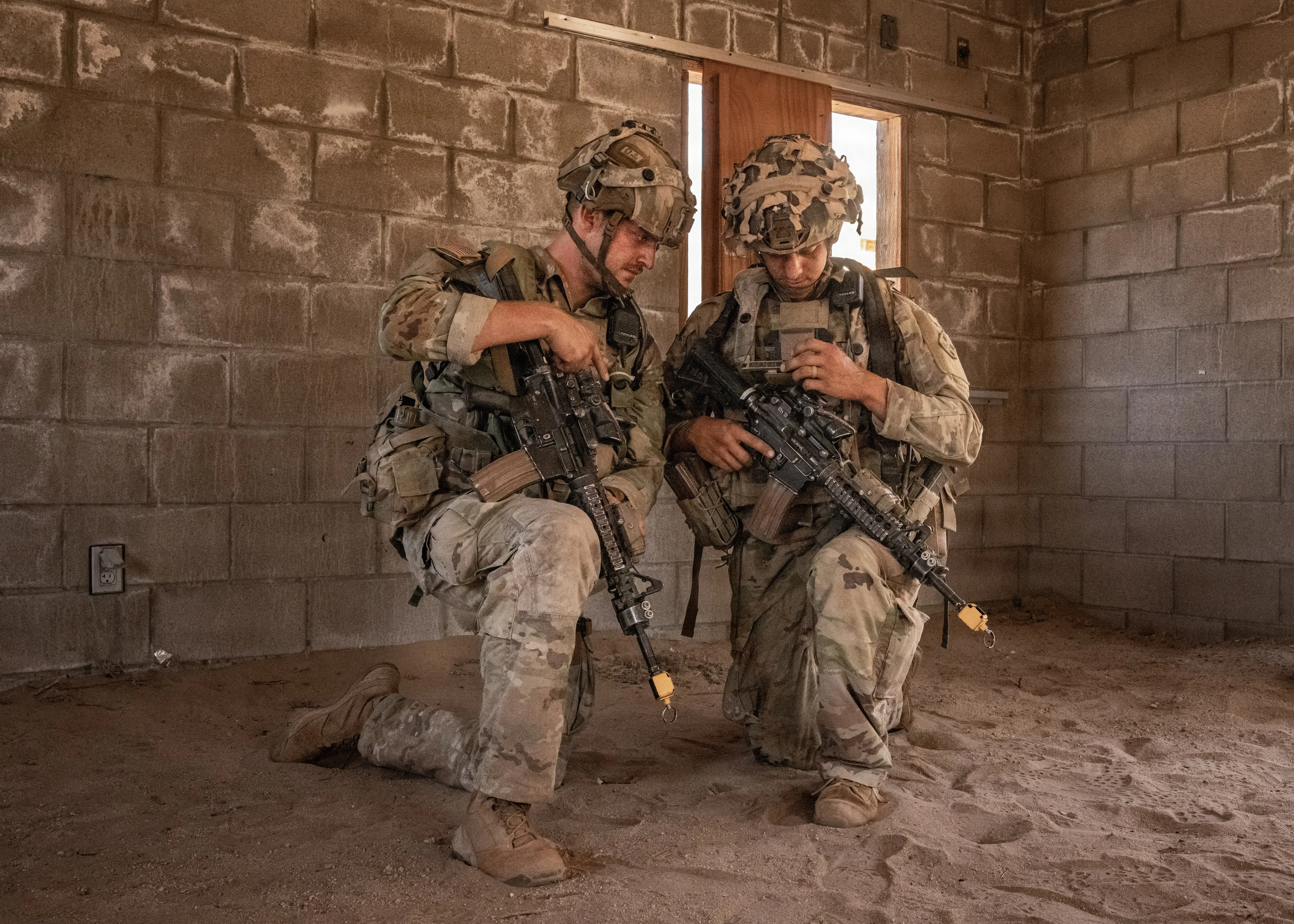 Two soldiers kneel inside a building looking at a small tablet that's attached to one of the soldiers' chests.