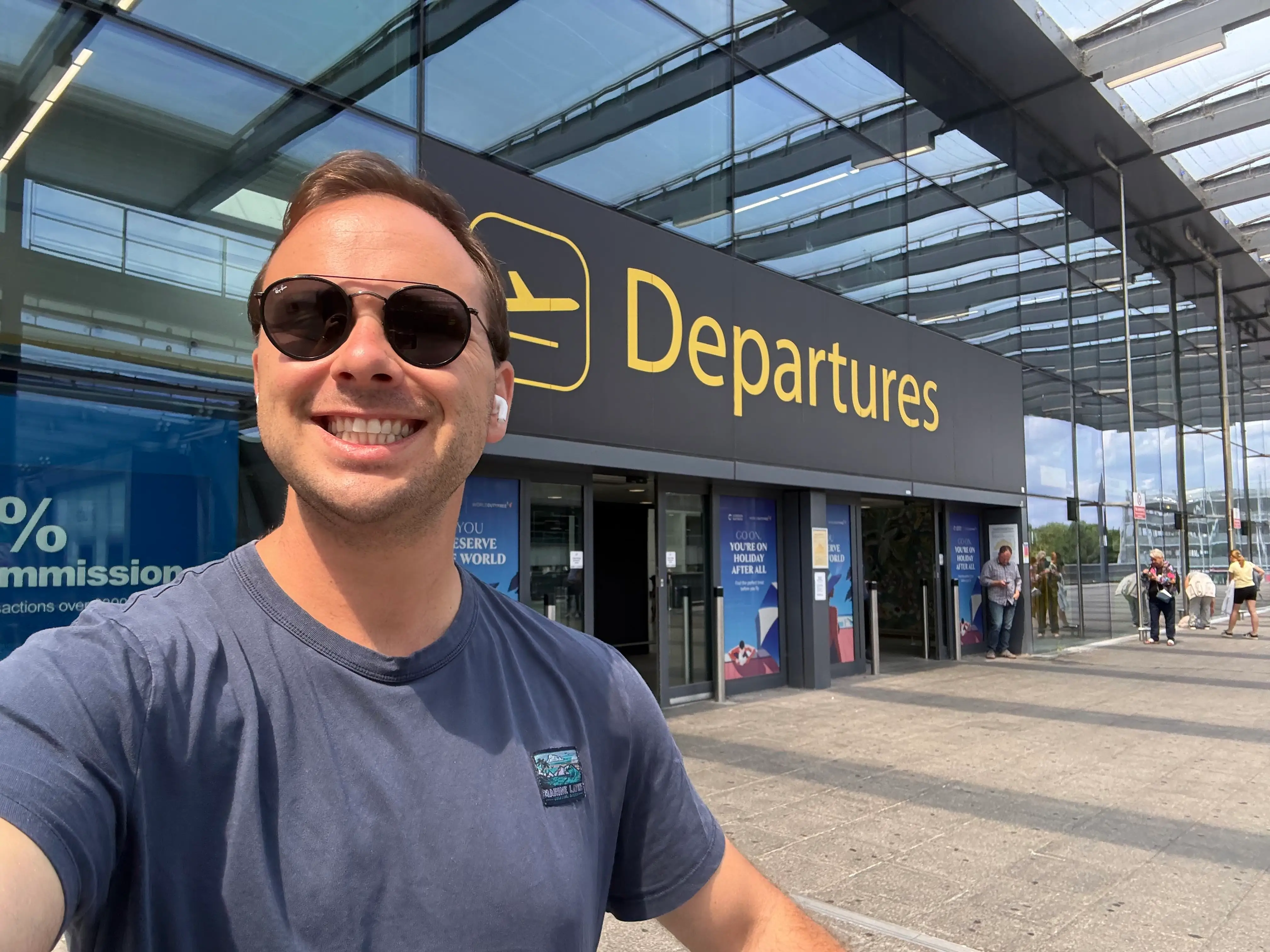 Author in a gray shirt and sunglasses in front of the airport depatures building.