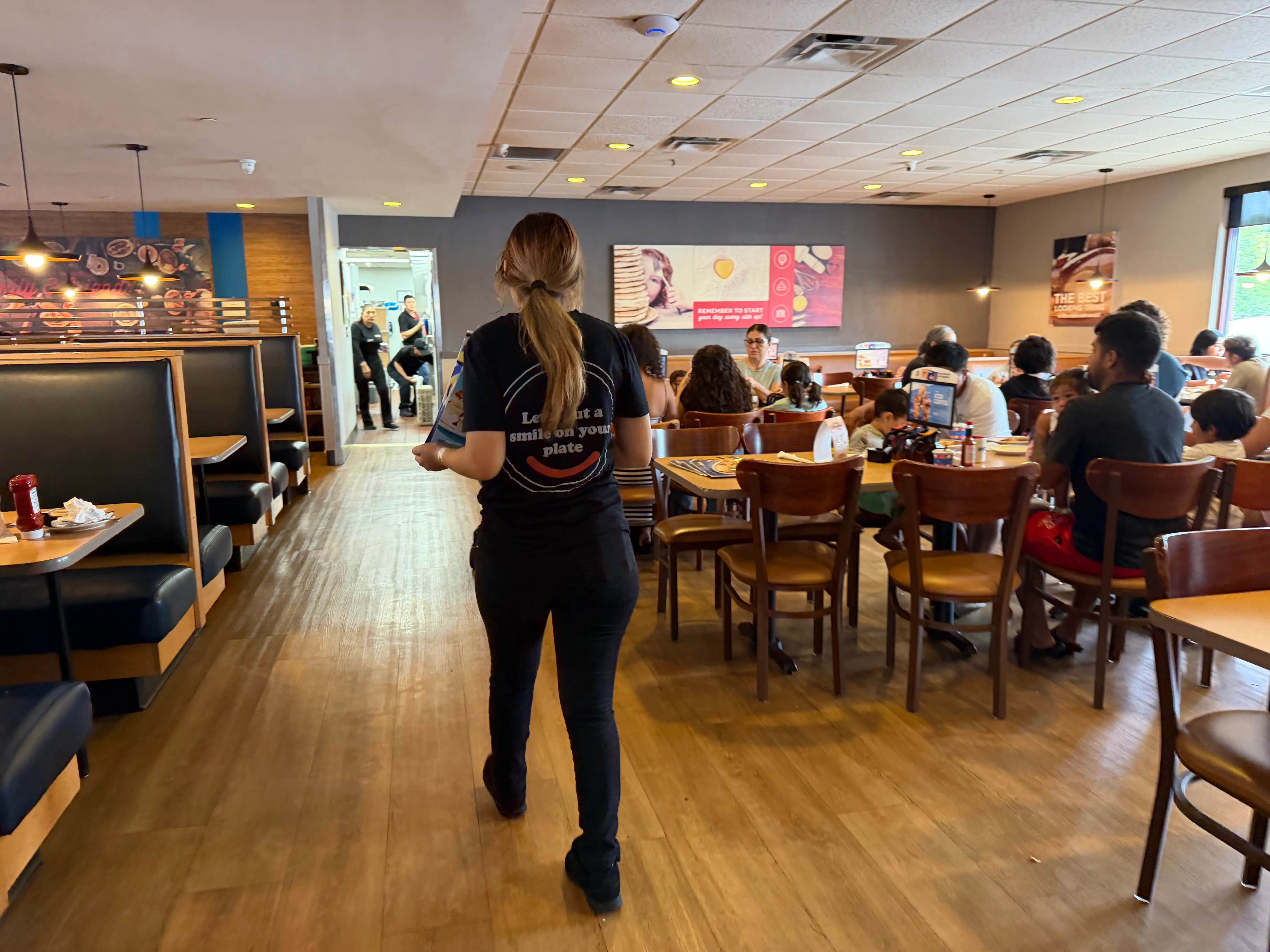 Server in IHOP shirt walking away, people sitting at tables in an IHOP