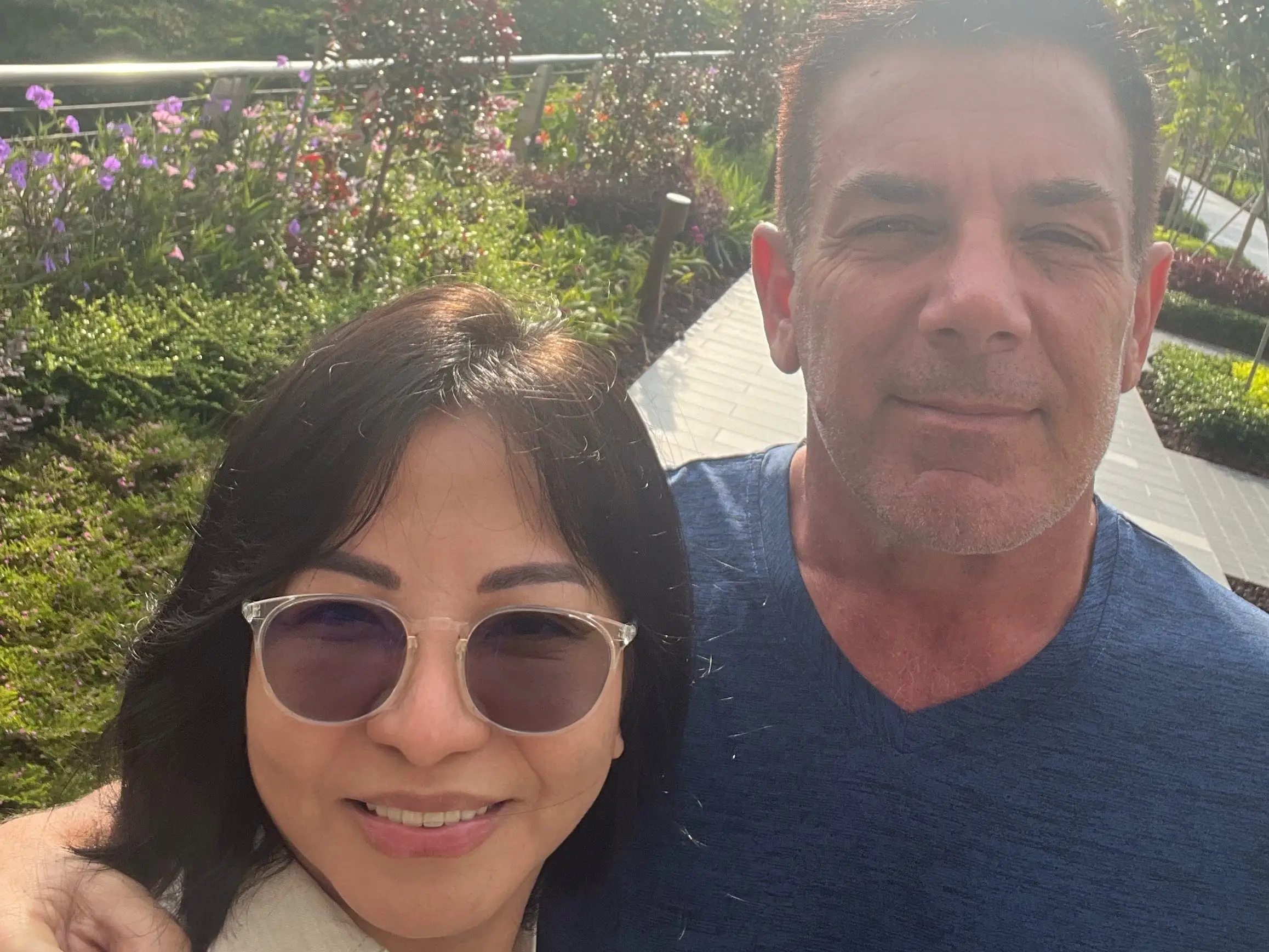 A middle-aged man and a woman standing in front of gardens.