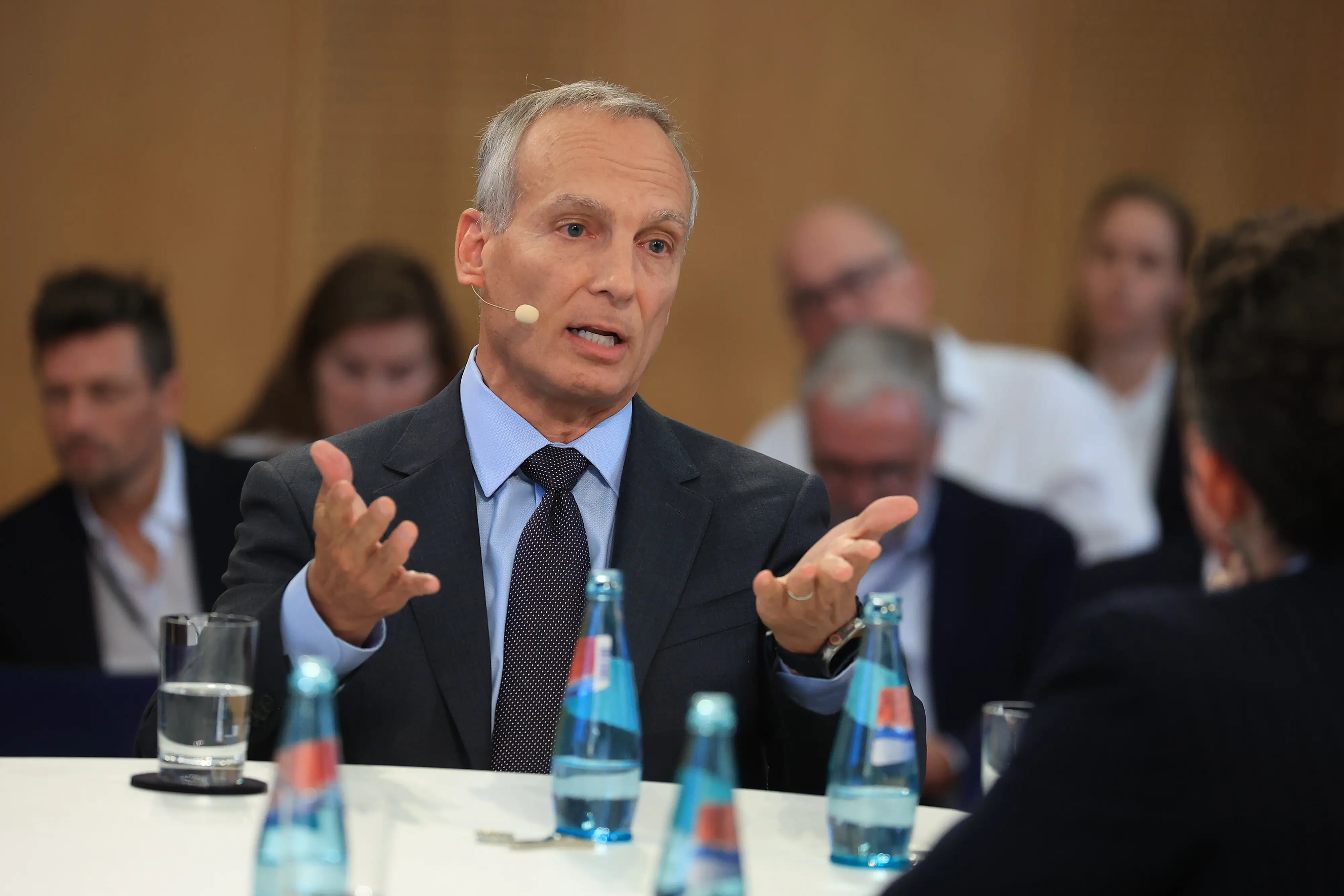 Booking's CEO, Glenn Fogel, puts his arms out as he speaks at a table.