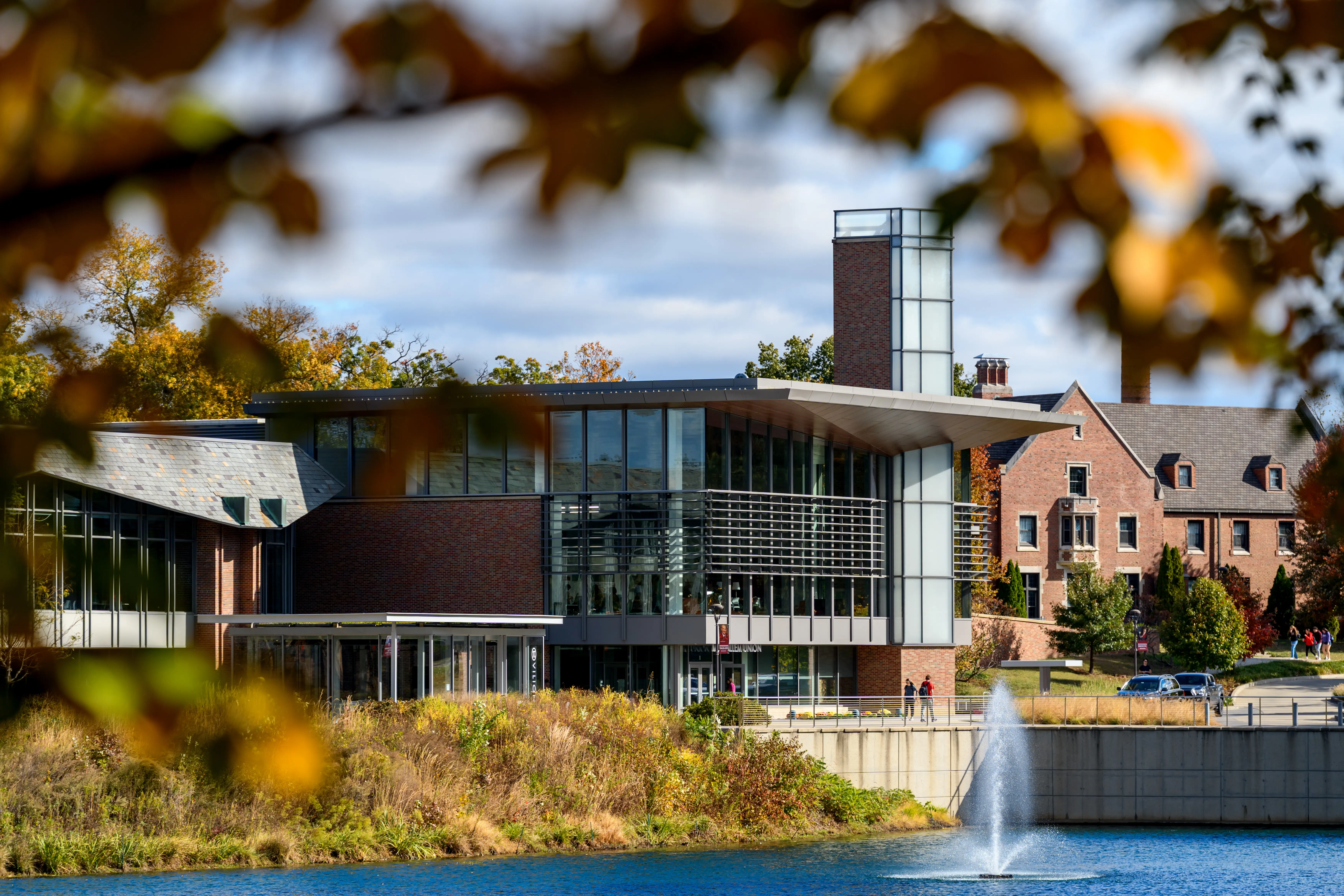 Modern brick and glass Rose-Hulman Institute of Technology building stands beside a pond with a fountain and autumn foliage.