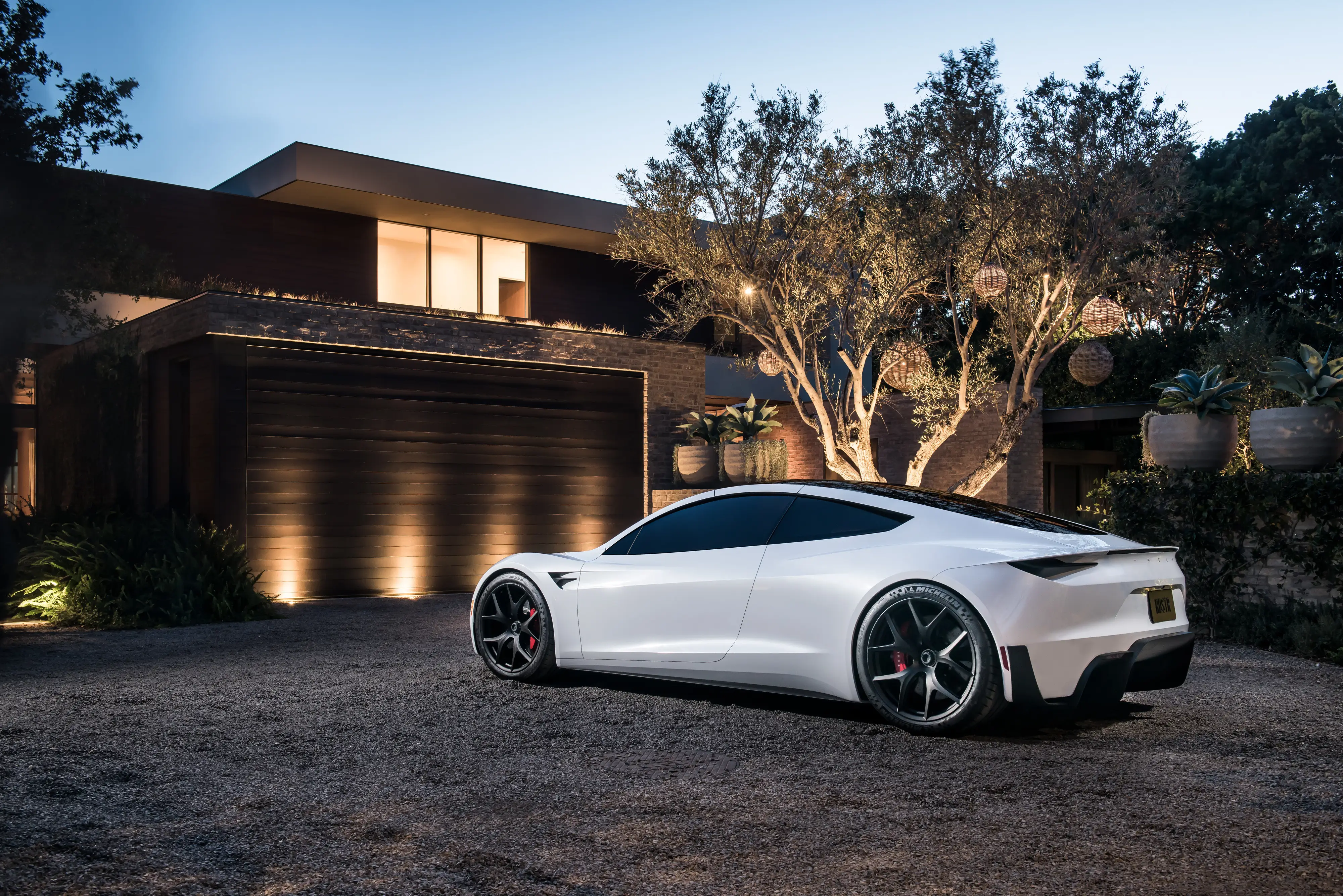 A prototype of a white Tesla Roadster parked outside a modern home.
