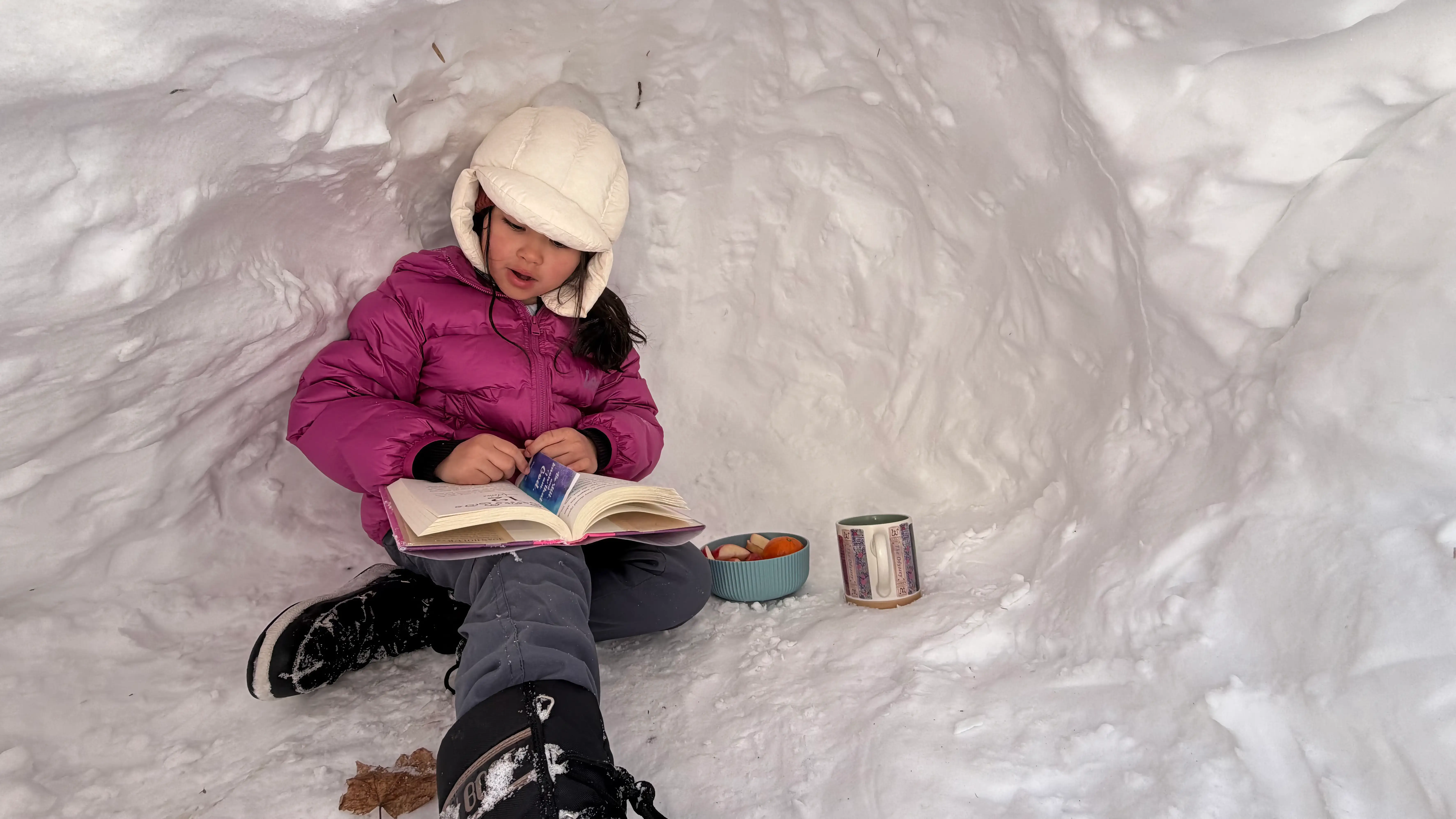 The author's granddaughter reads while inside a snow fort.