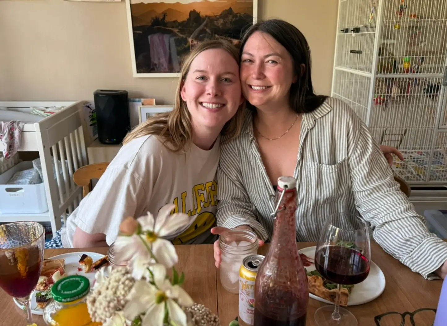 The writer and her partner posing next to each other while eating pizza at a table in their house.