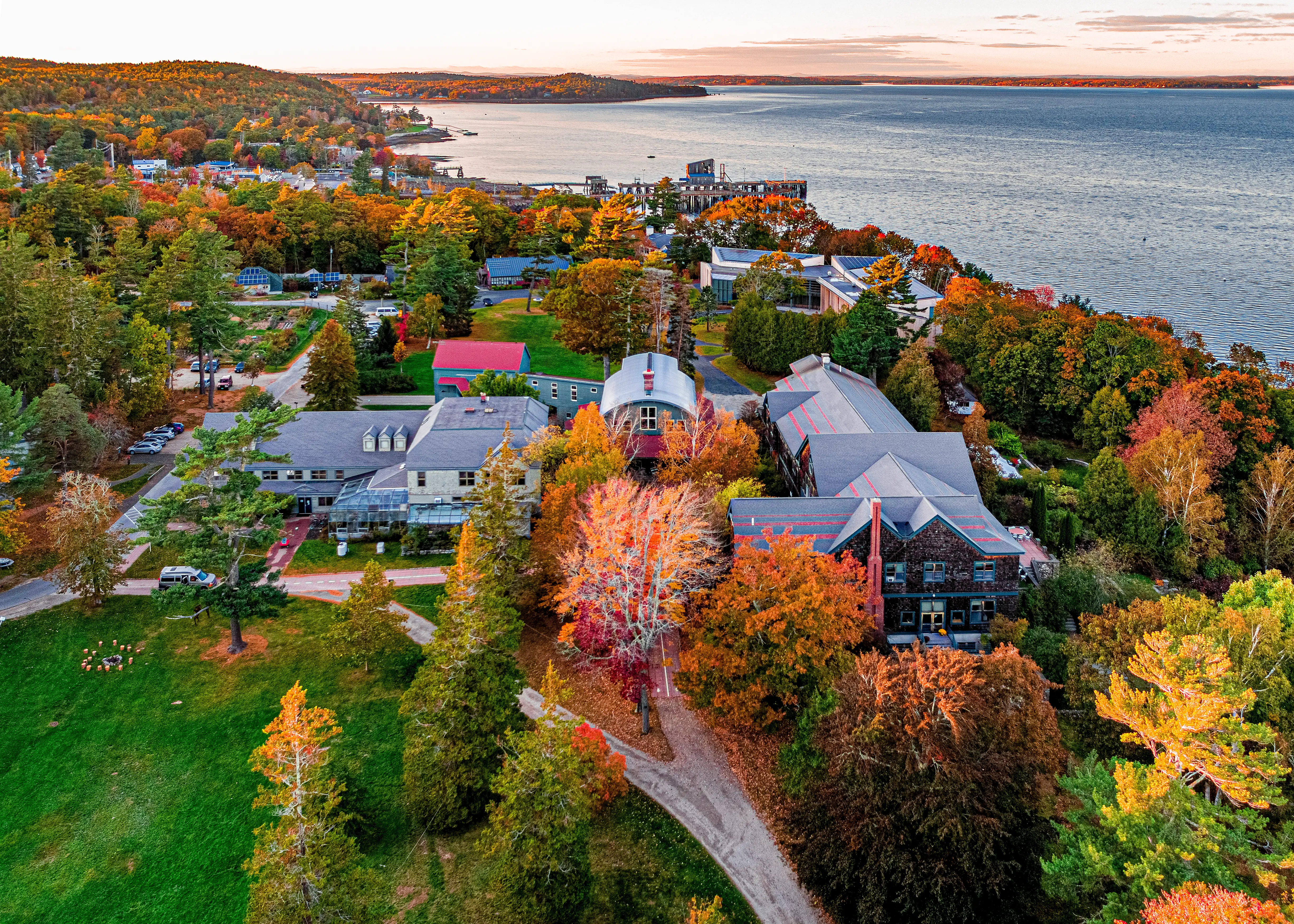 Aerial view of College of the Atlantic with autumn trees, buildings, and a pier beside a large body of water.