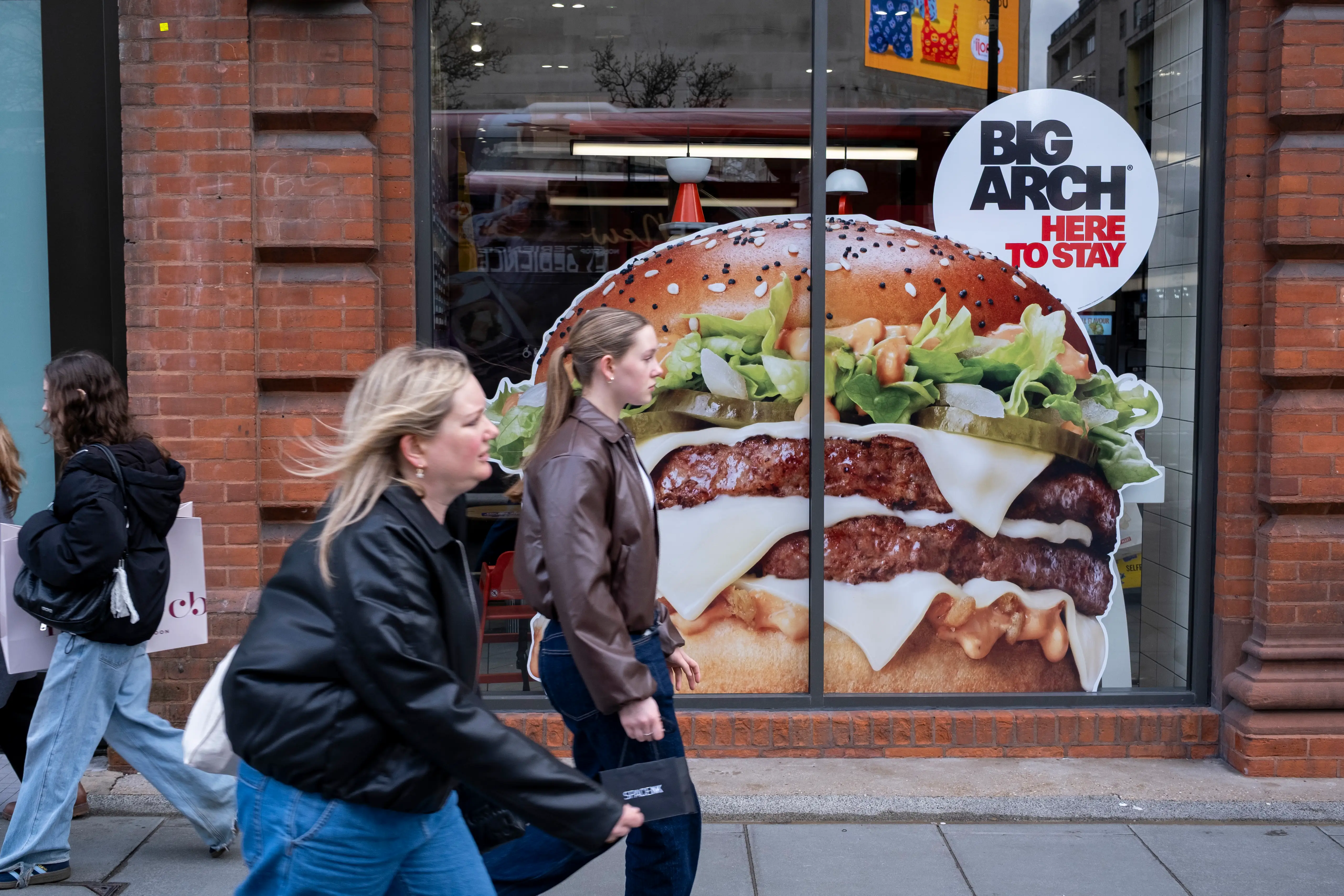 Two blond women walk by a McDonald's restaurant with an ad featuring a burger that reads: 