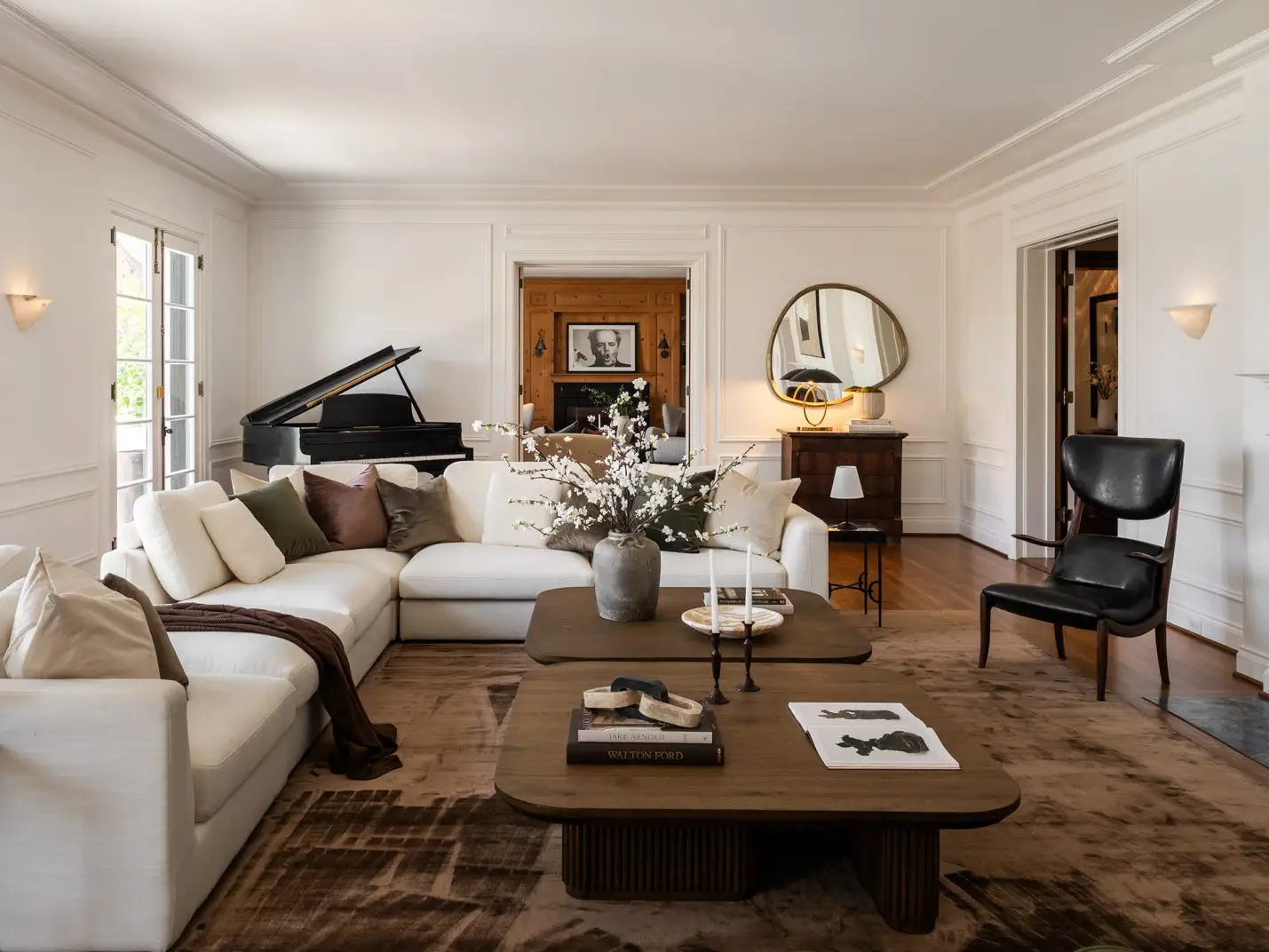 Elegant living room with cream sectional sofa, grand piano, fireplace, coffee table, and French doors.