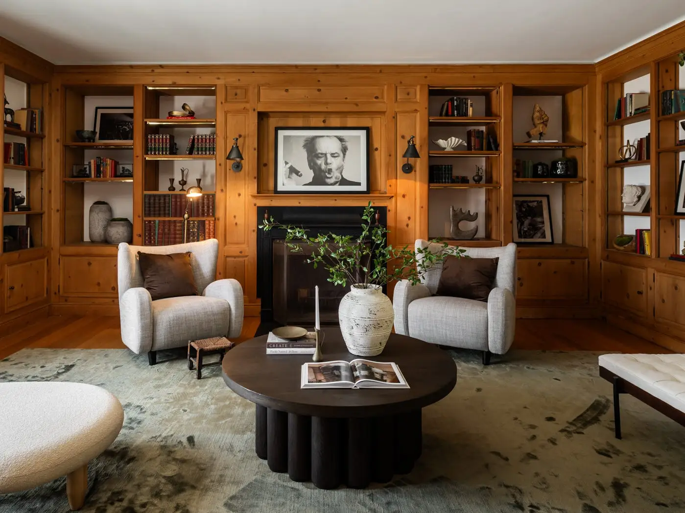 Wood-paneled library with built-in shelves, armchairs, a fireplace, coffee table, and an Albert Einstein portrait.
