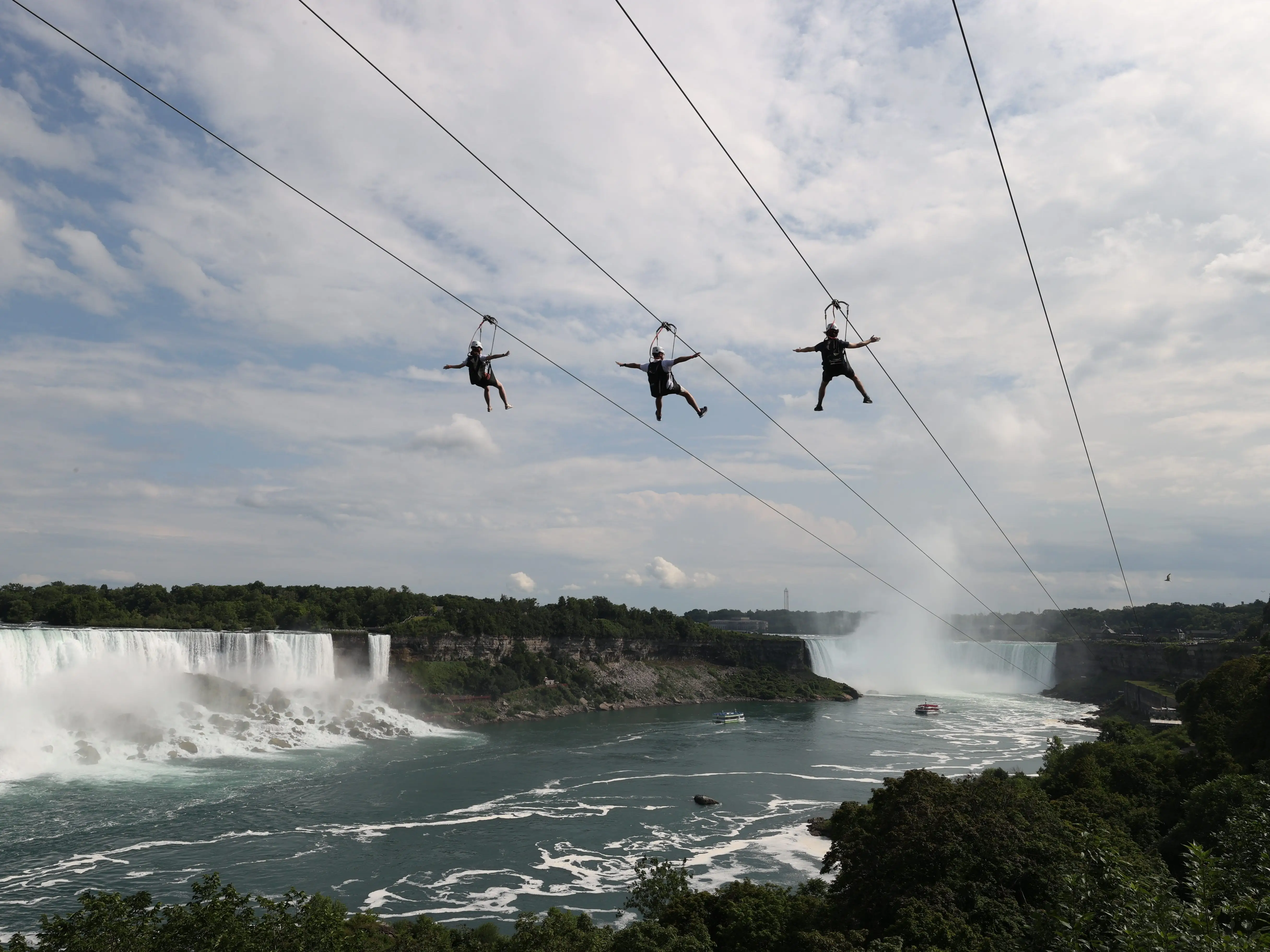 Three people riding a zip line over Niagara Falls.