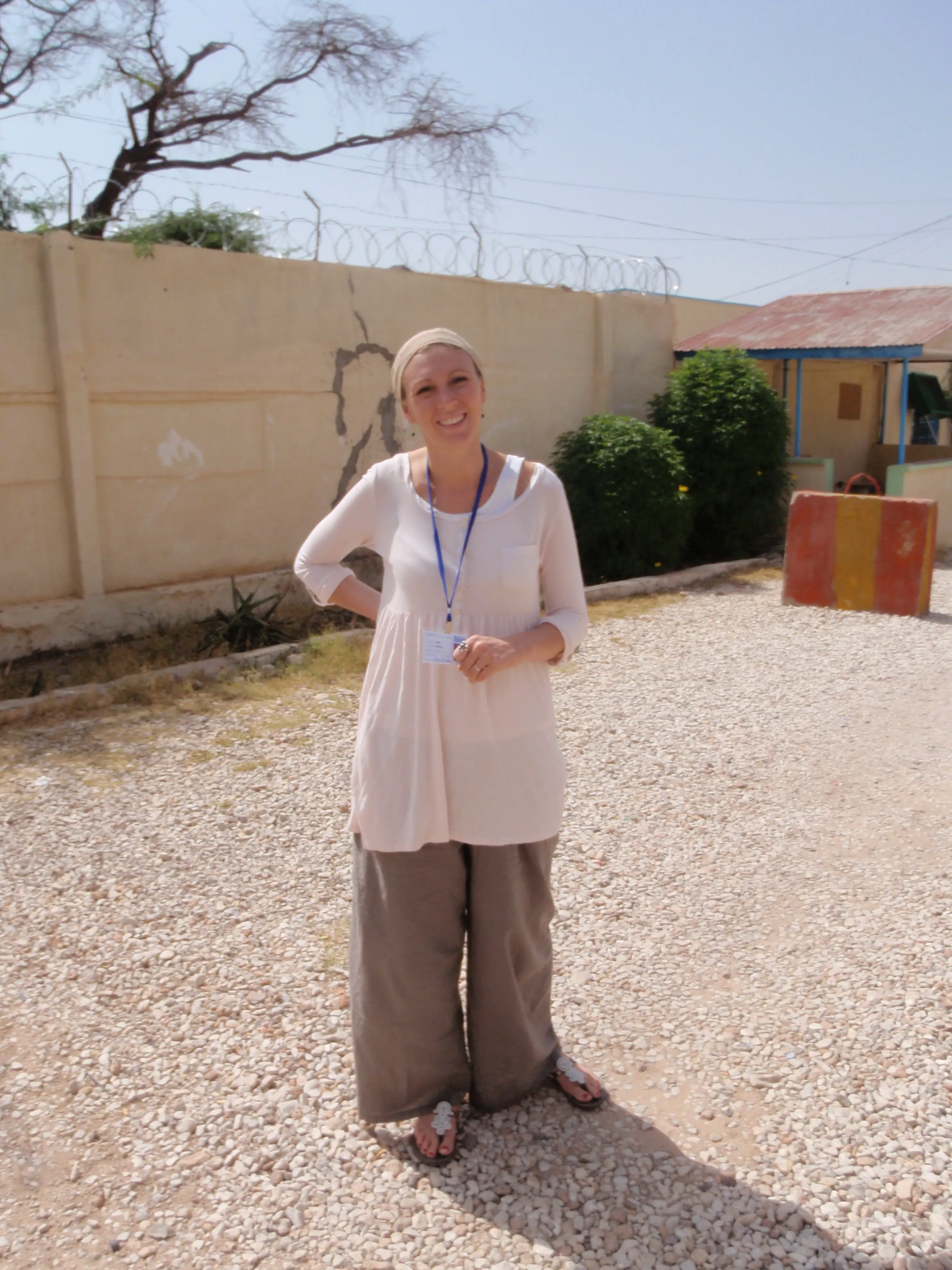 Jessica Buchanan is in a long white shirt, brown pants, and sandals, standing outside at the school where she teaches.