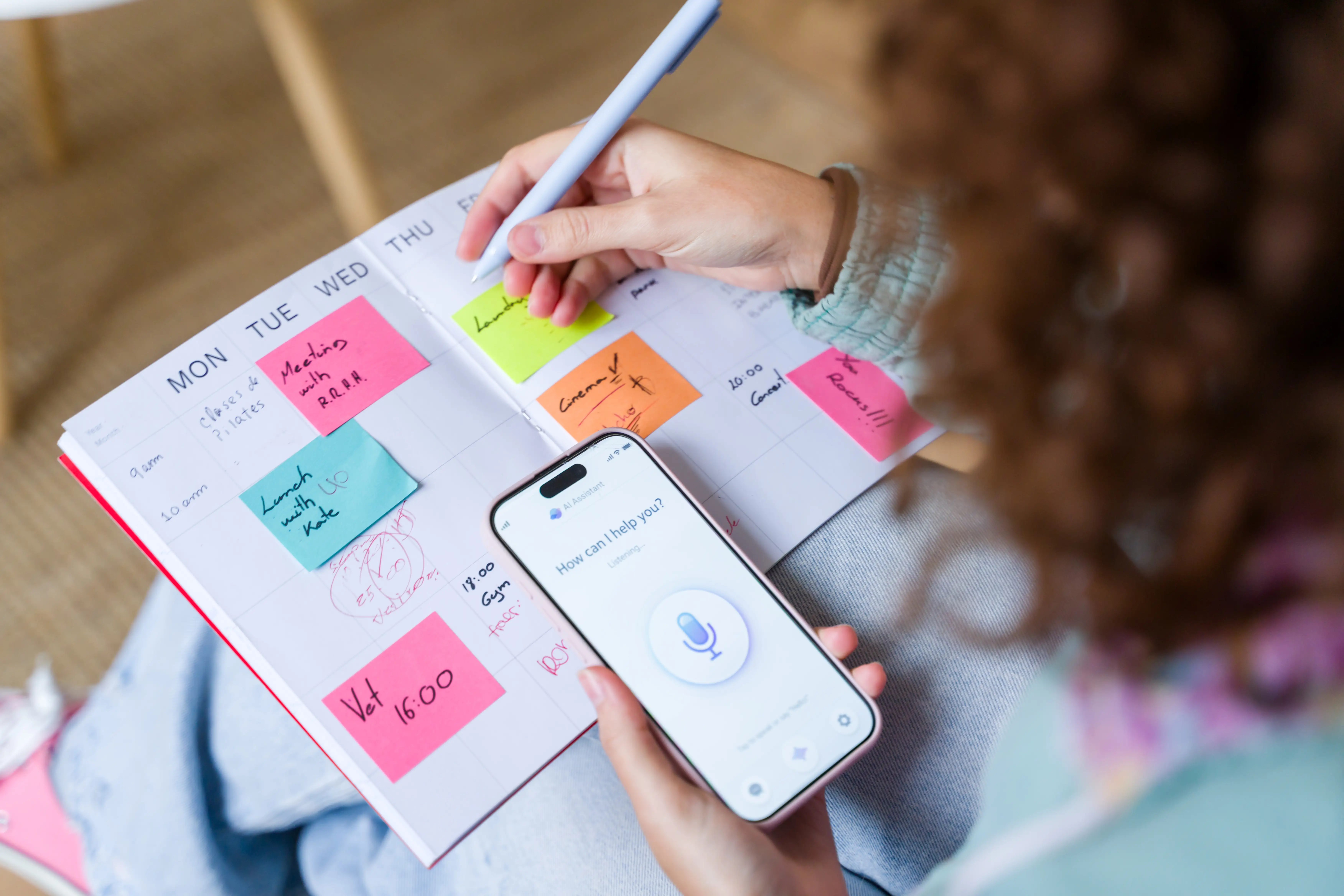 A woman is using an AI assistant on her phone while she looks at a planner.