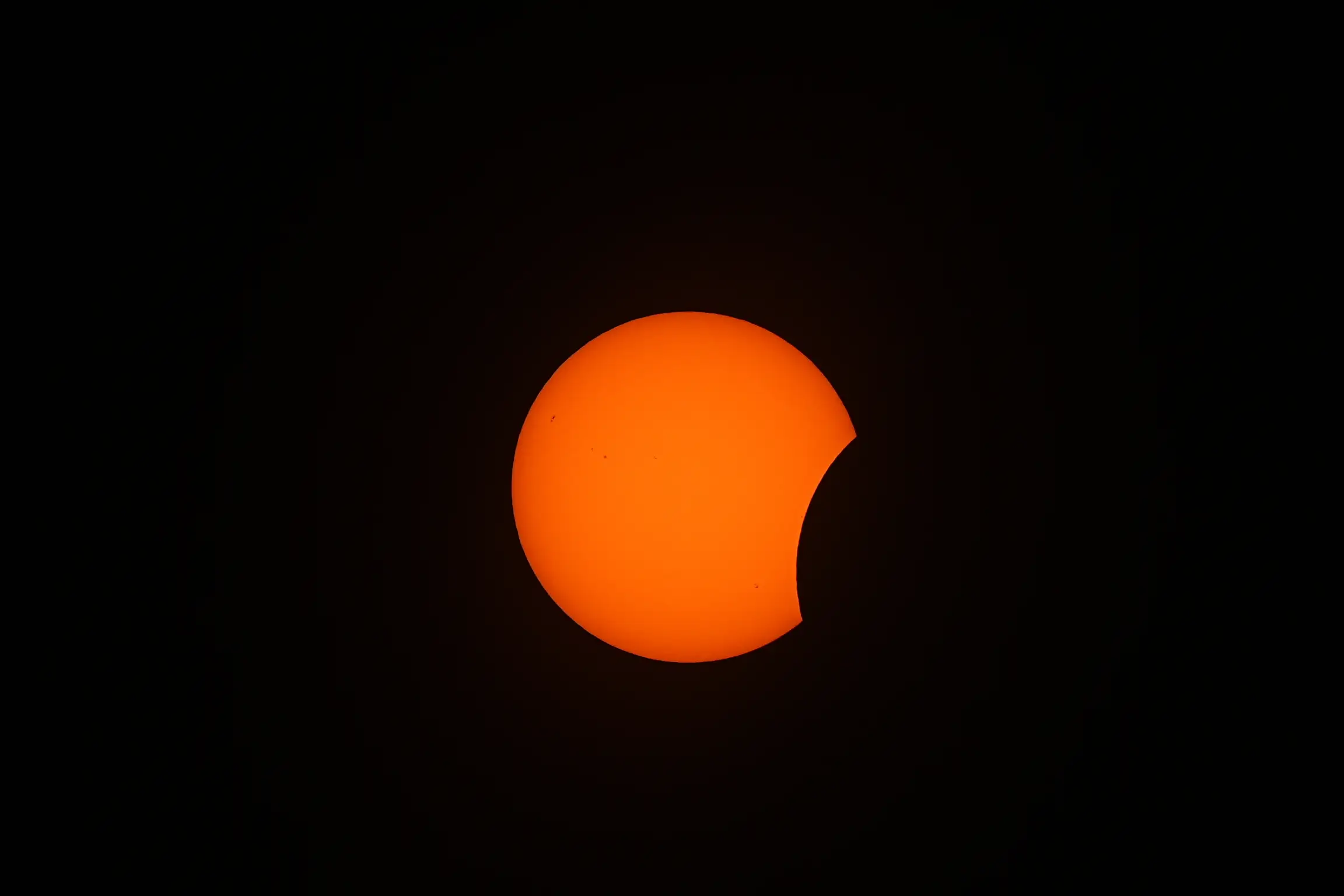 The moon begins to pass over the bright orange sun.