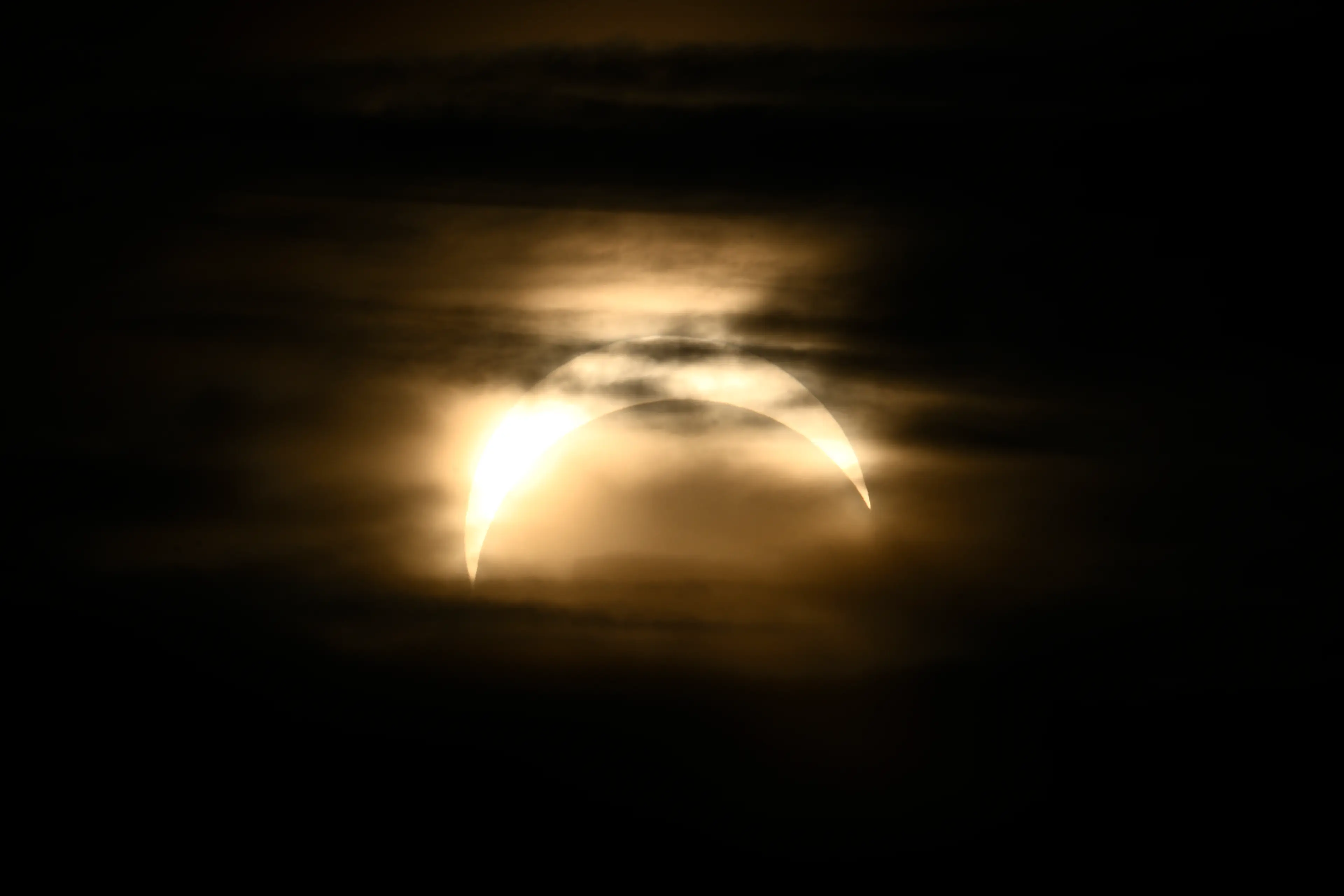 The moon passes over the sun during a partial eclipse, with a few clouds slightly obscuring the view.