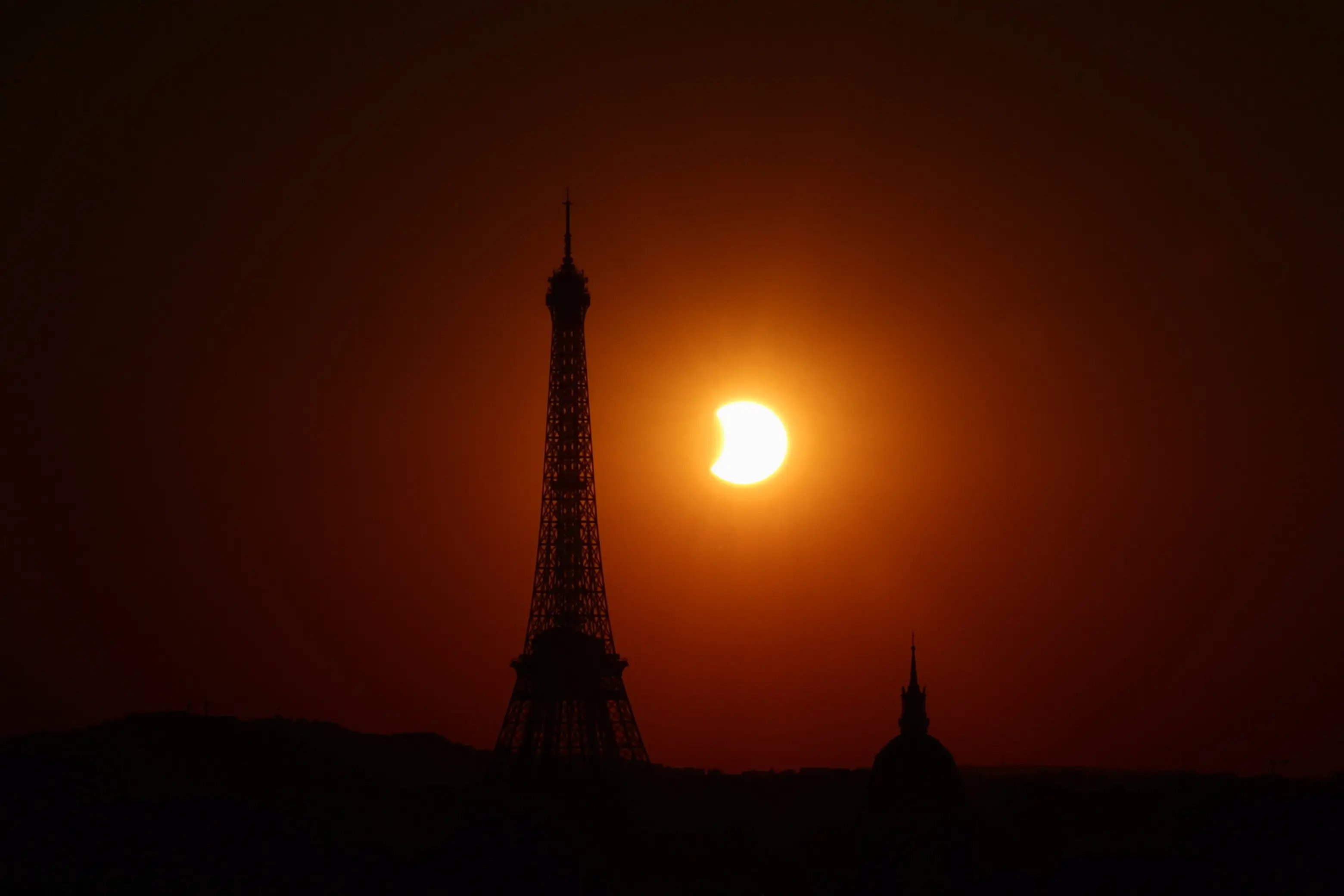 The moon passes over the sun to the right of the Eiffel Tower.