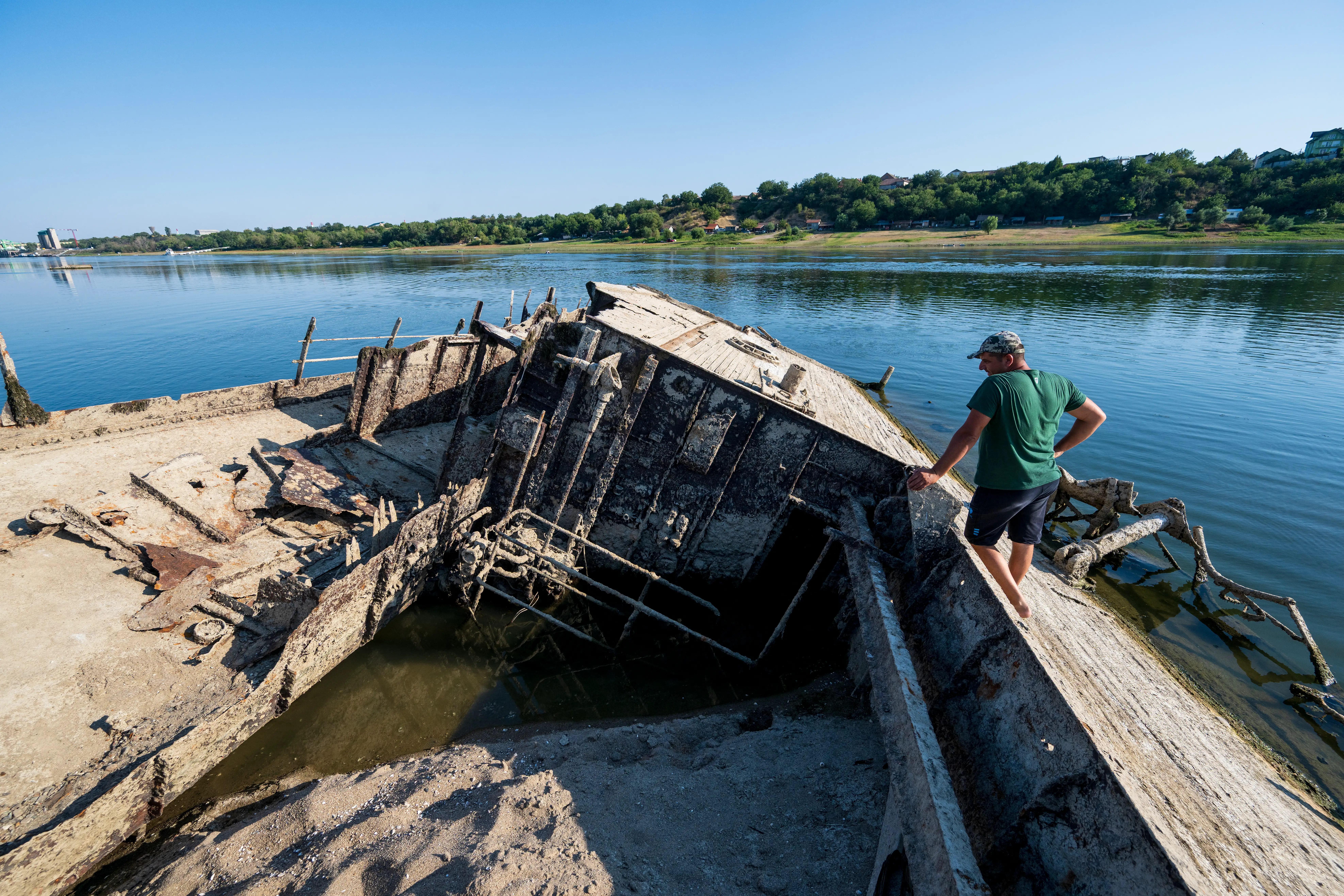 A man stands next to an unearthed World War II ship that was unearthed in a river.