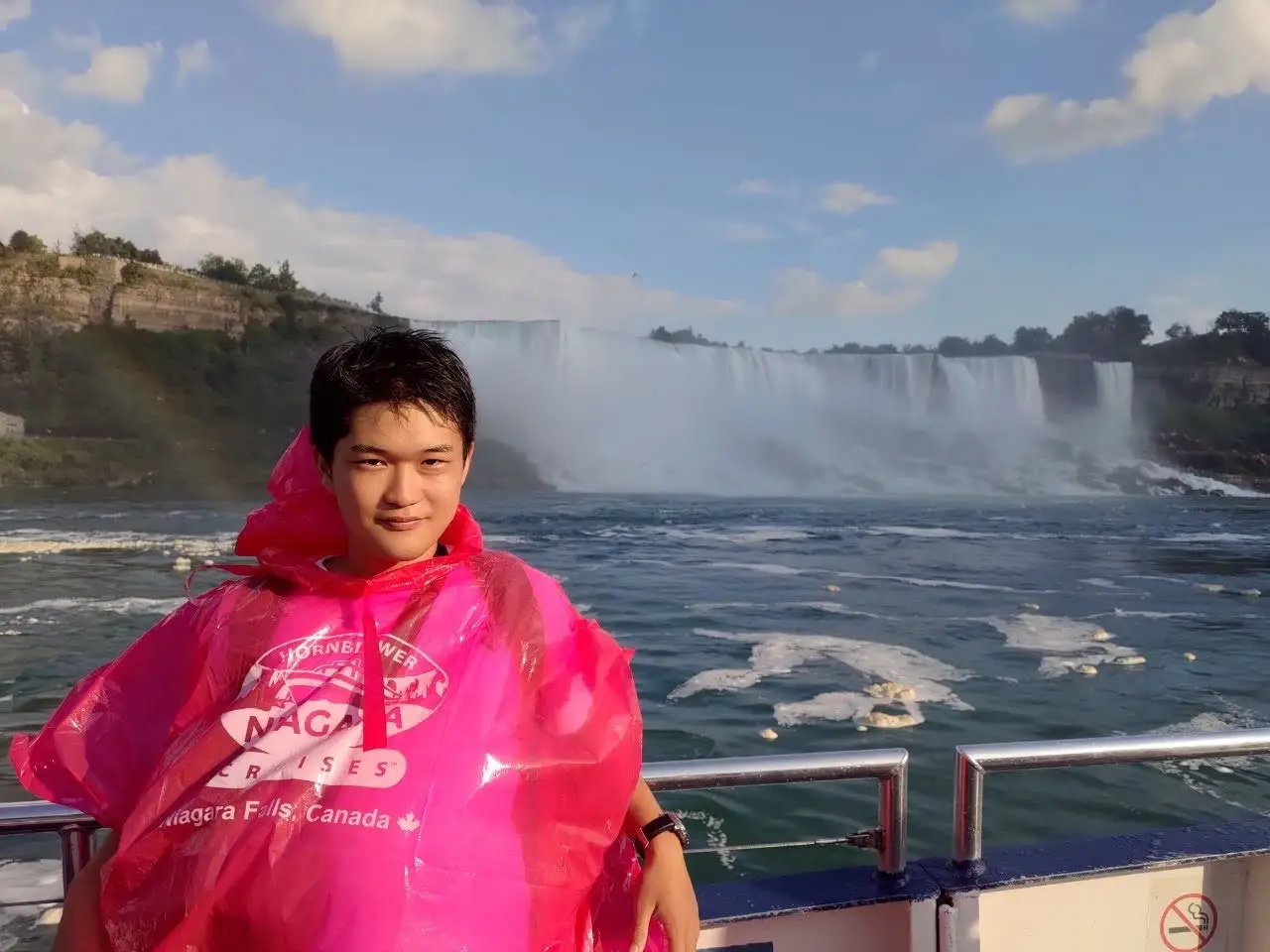 A man in a pink poncho posing with the Niagara Falls, in Canada, in the background.