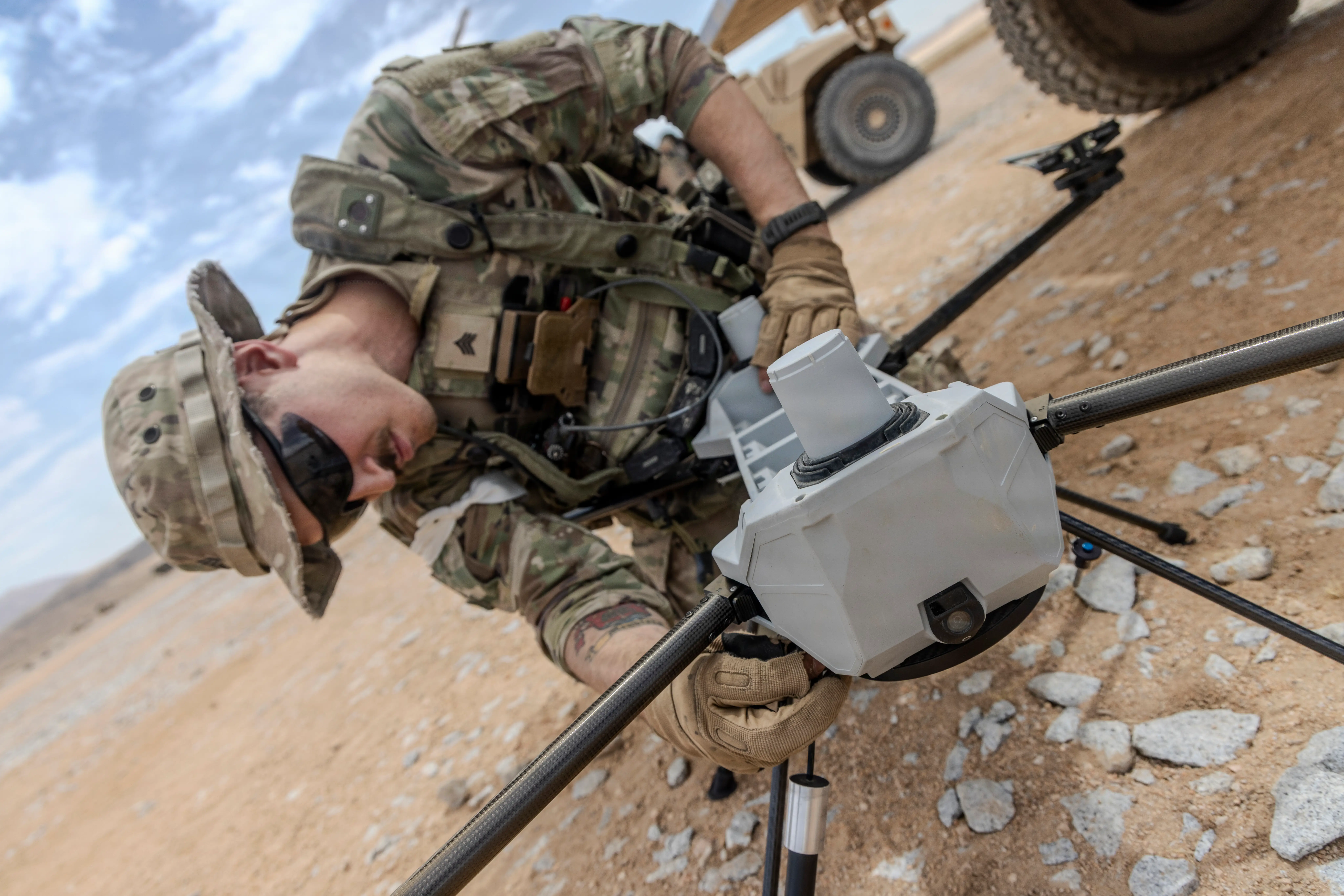 A US Army soldier works on a drone sitting on the ground in the desert.