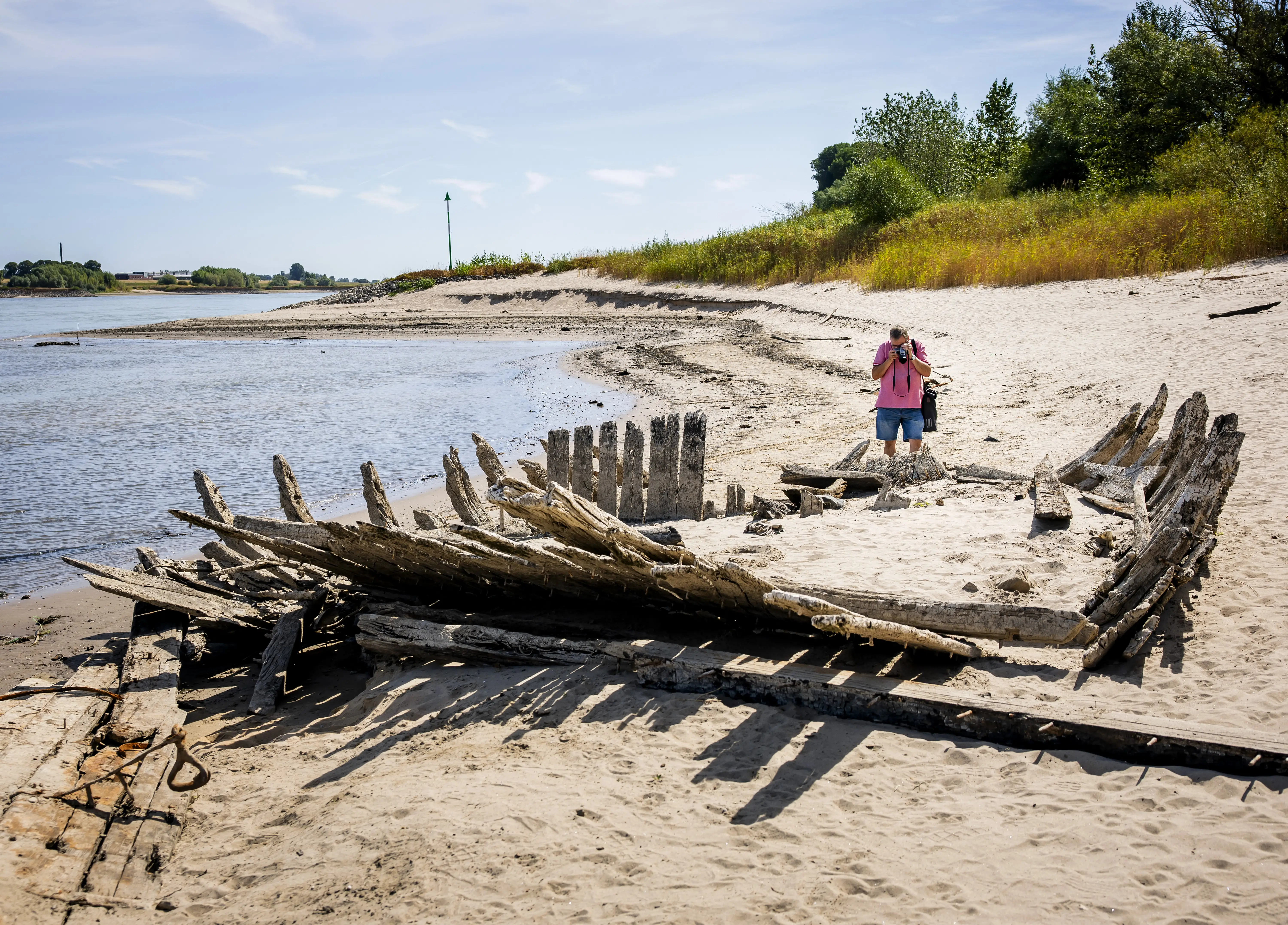 A man stands before an old shipwreck on a beach.