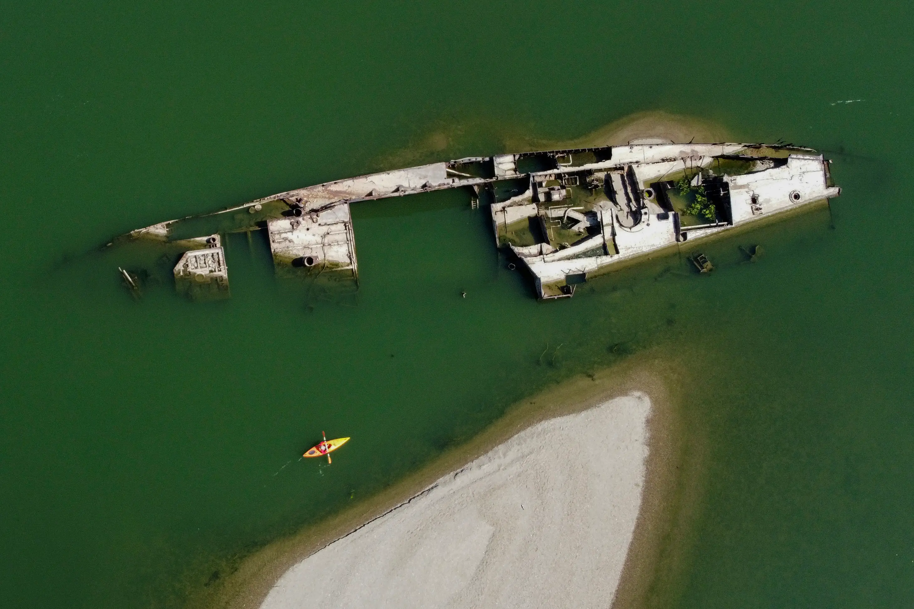 A sunken ship lies in a green riverbed.