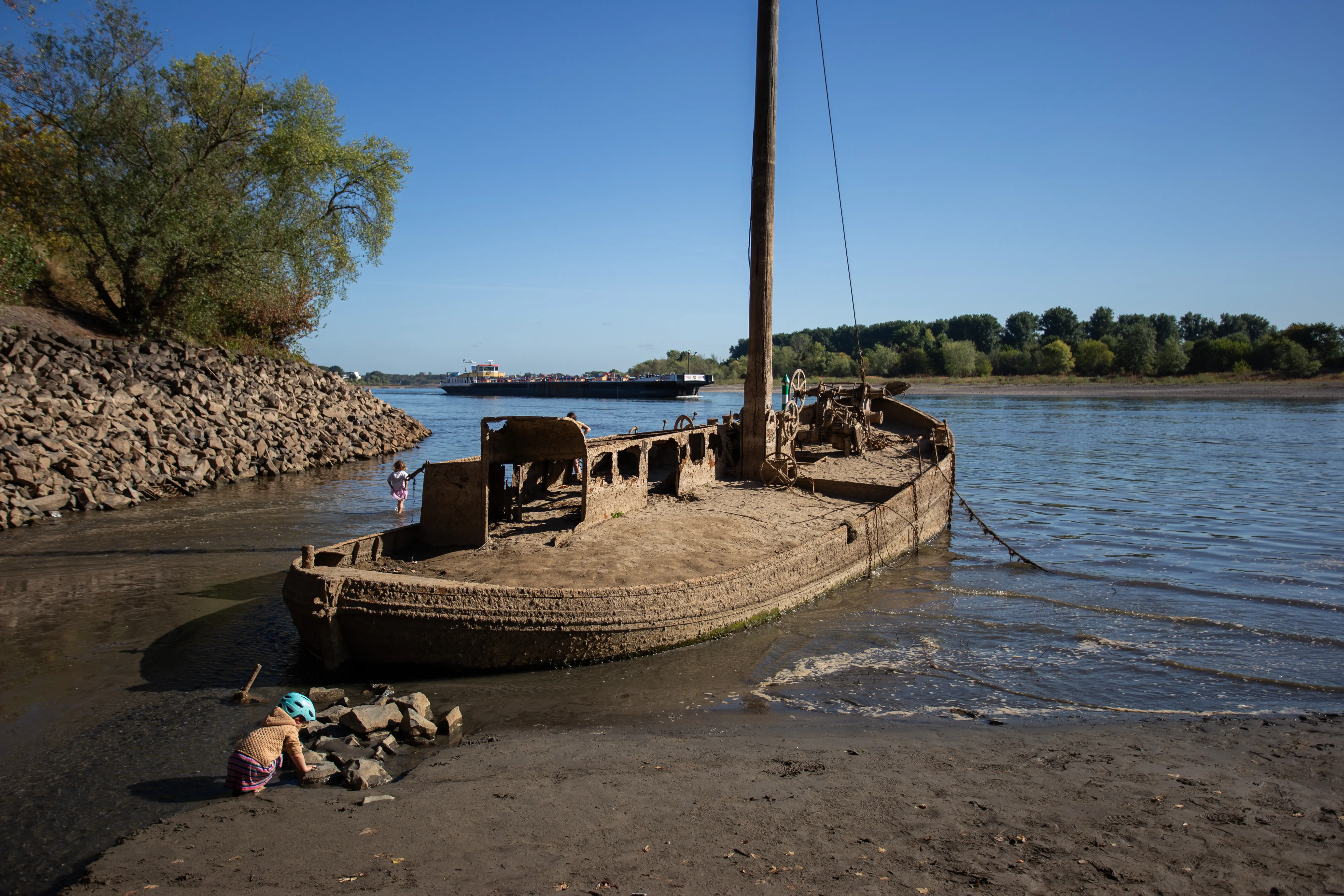 Two children play next to an old, sunken ship in a dry river.