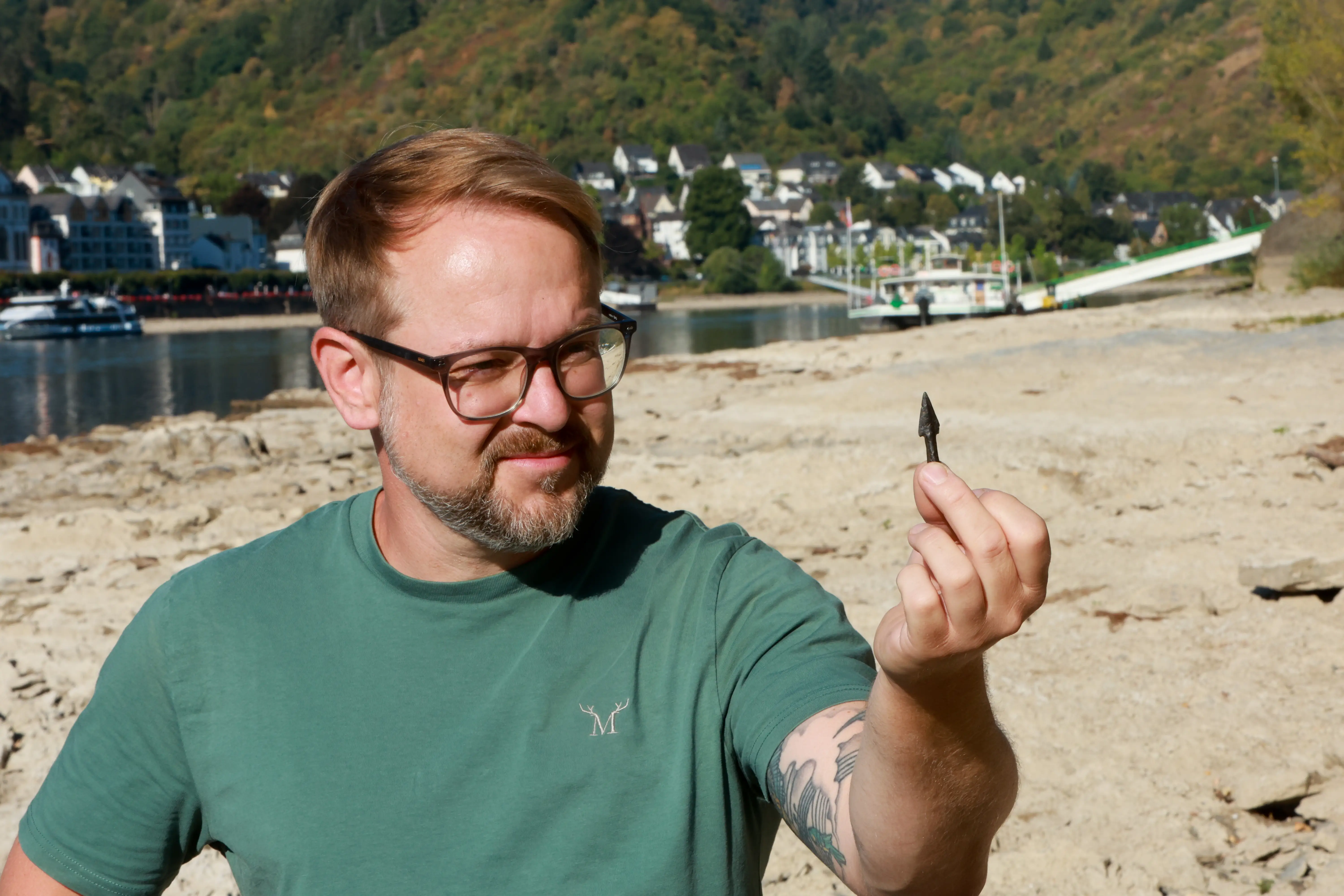 A man holds up an arrowhead while standing on a dry riverbed.