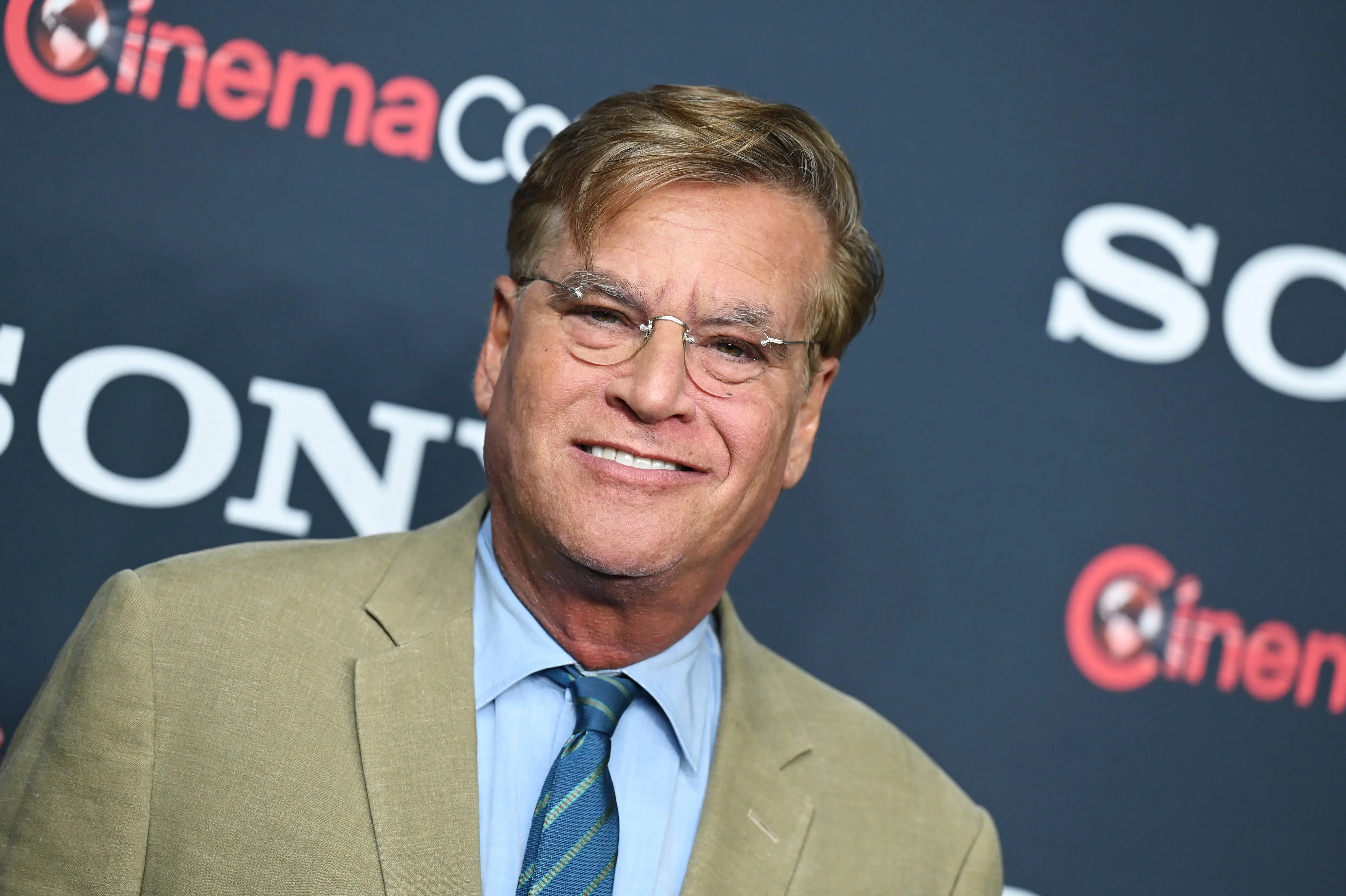 Writer Aaron Sorkin stands on a red carpet.