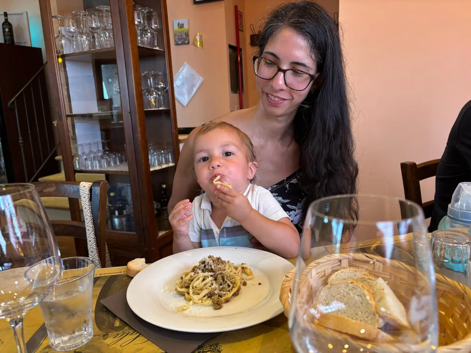 The author's son eats pasta at a restaurant while sitting on her lap.