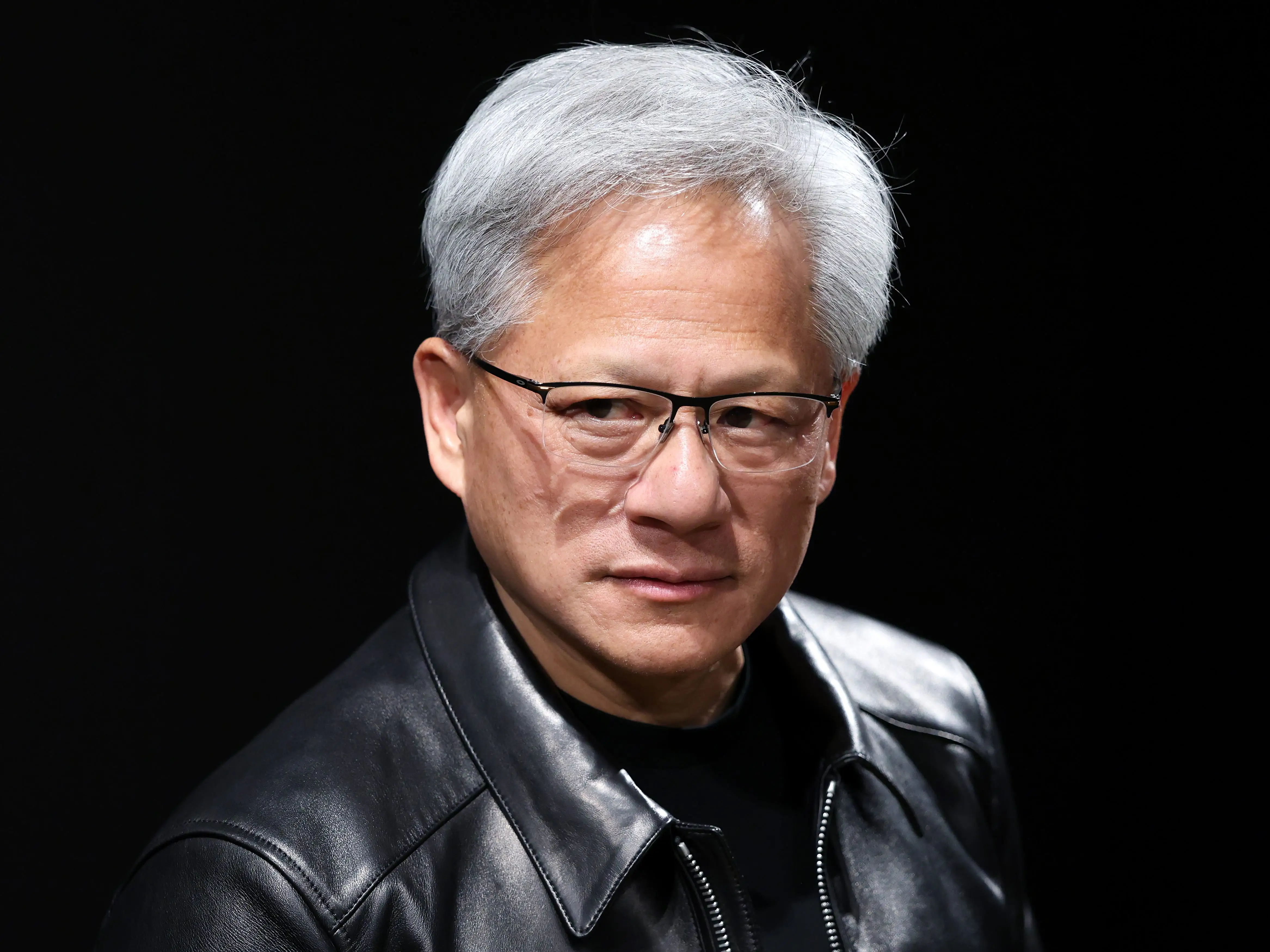 Nvidia CEO Jensen Huang in Japan, looking downward on stage, wearing a black leather jacket and glasses.