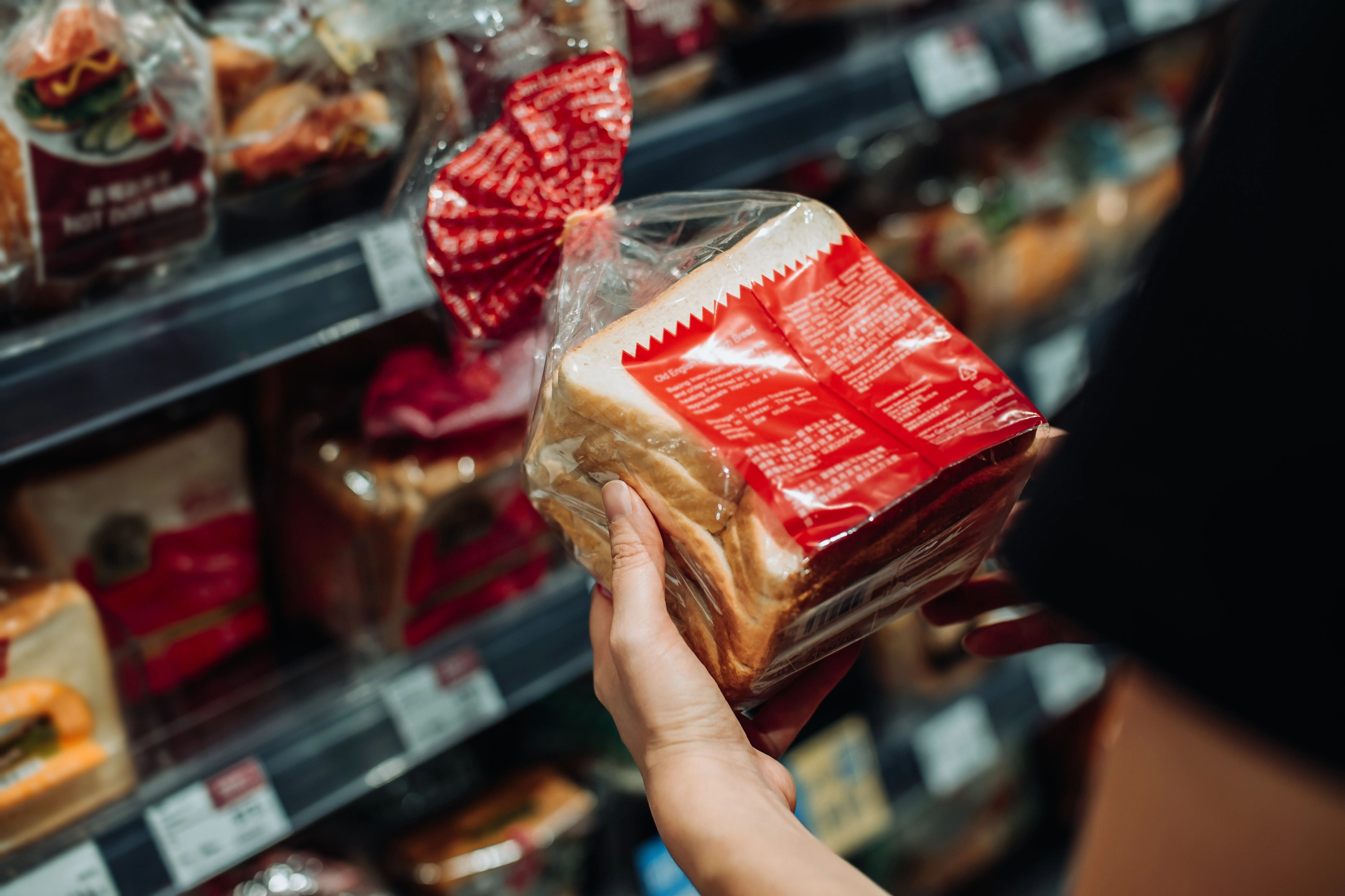 A shopper holds a packaged loaf of bread in a grocery store bakery aisle.