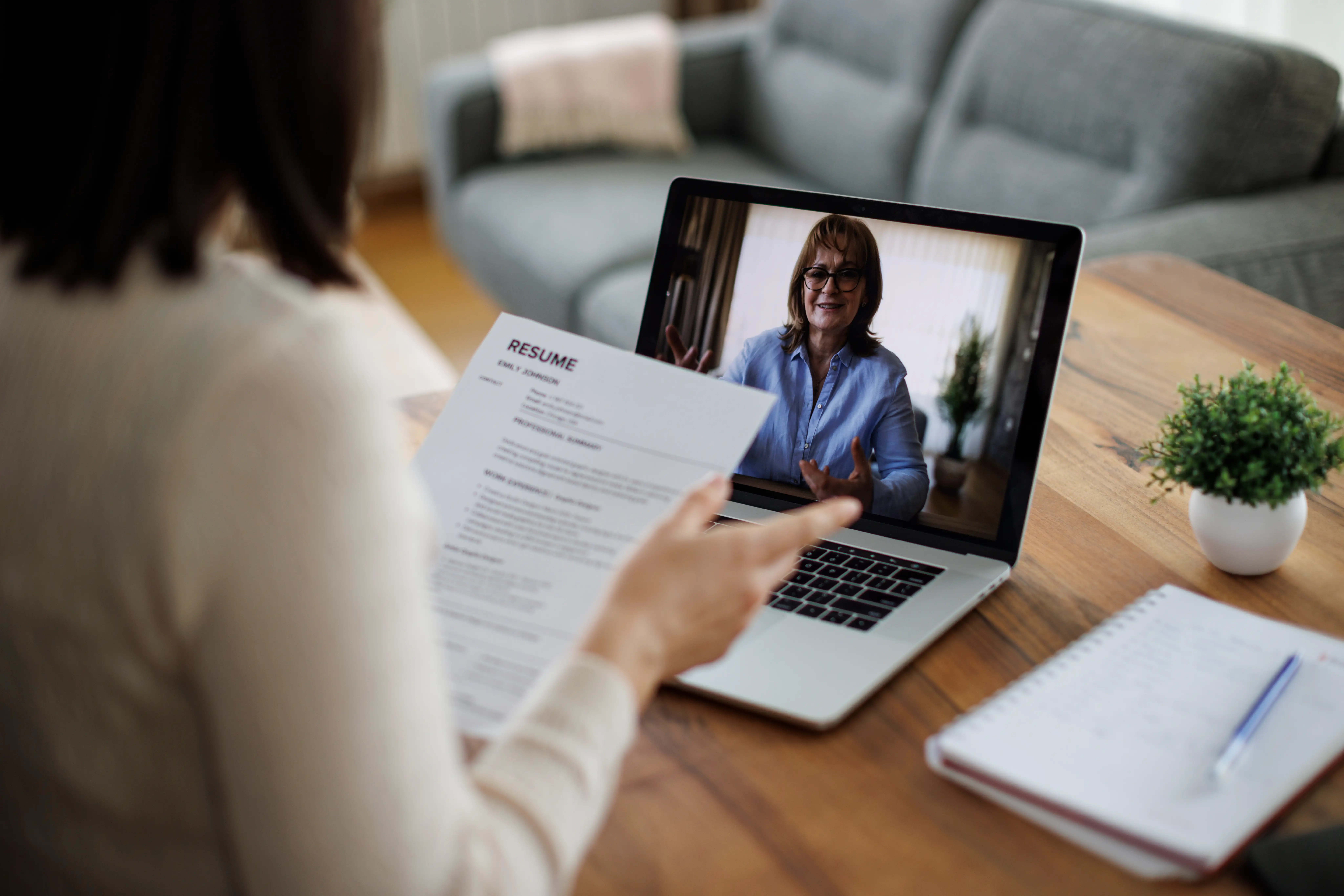 A person holds a resume during a video interview on a laptop at a wooden table.