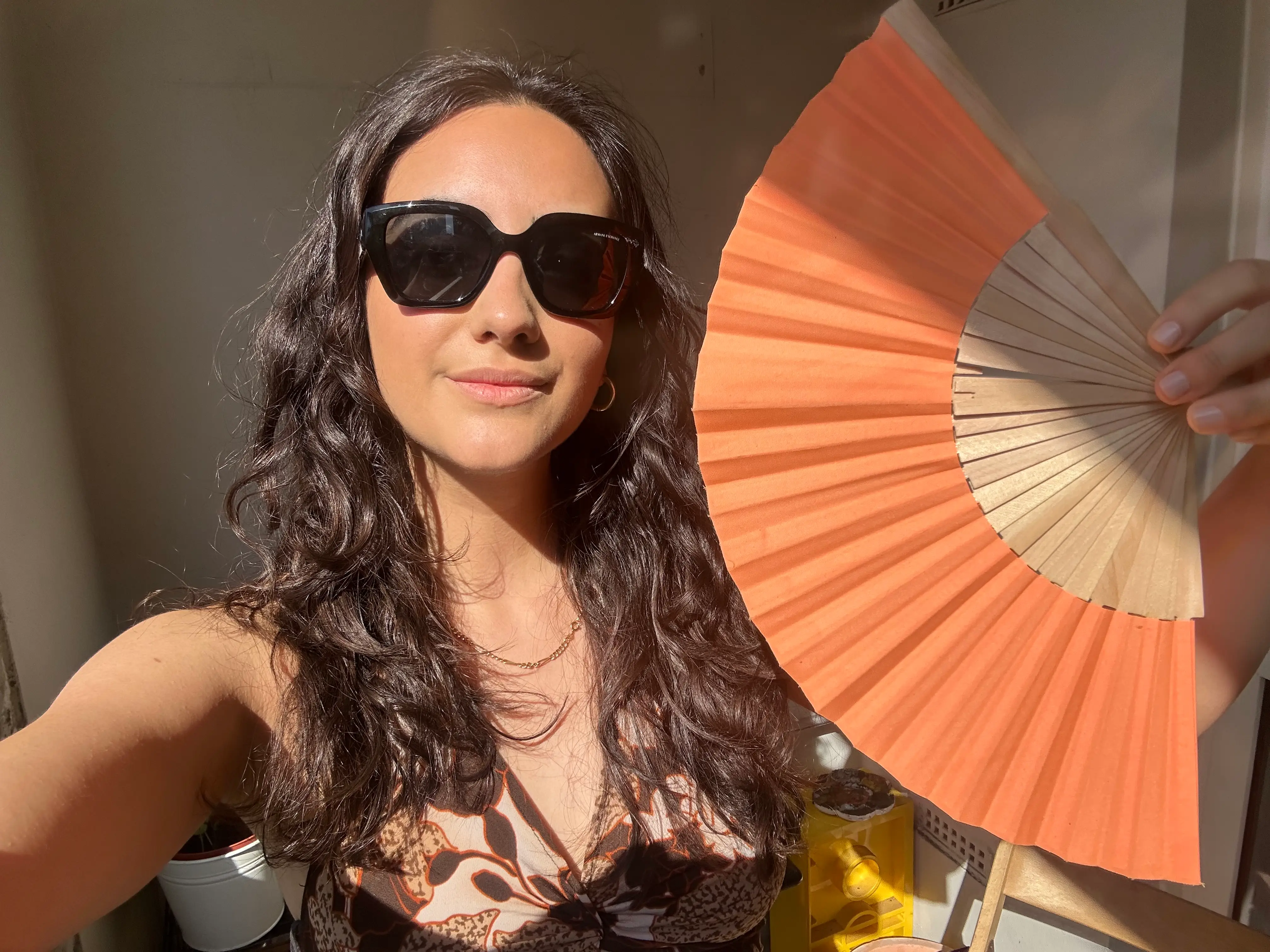 Roya Shahidi wearing sunglasses holding an orange handheld paper fan.