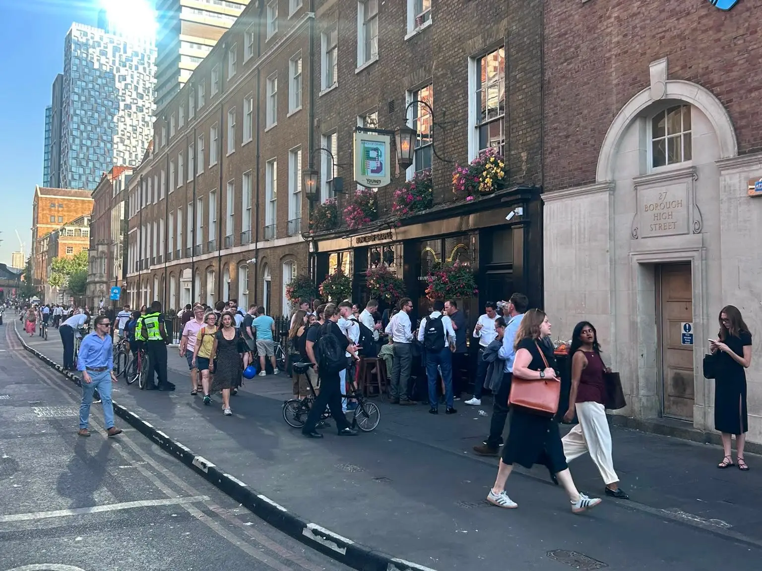 Crowds gather outside brick buildings on Borough High Street, with a Barclays logo and sunny city skyline visible.