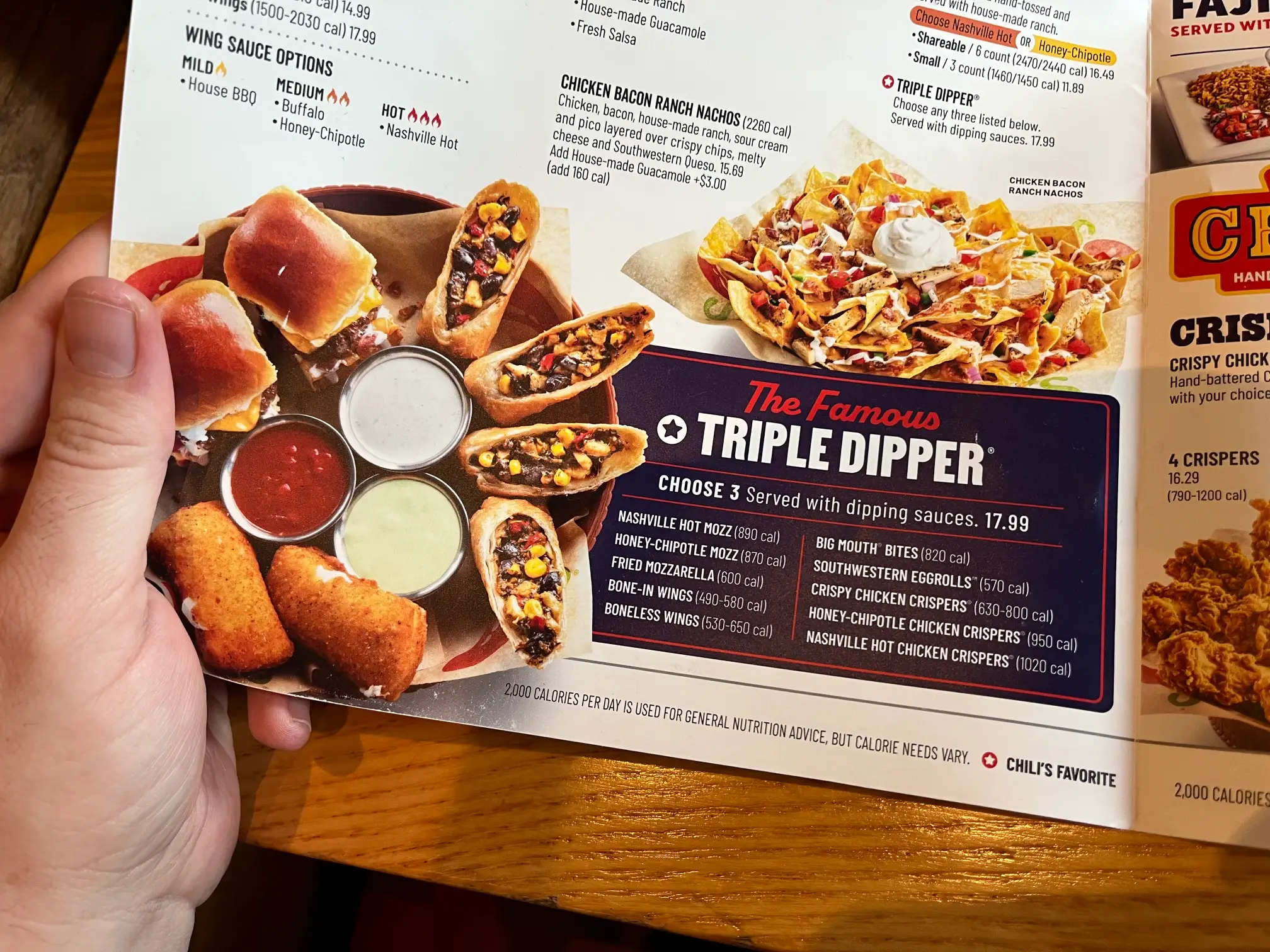 A hand holds an open Chili's menu showing The Famous TRIPLE DIPPER appetizer section with sauces and fried items.