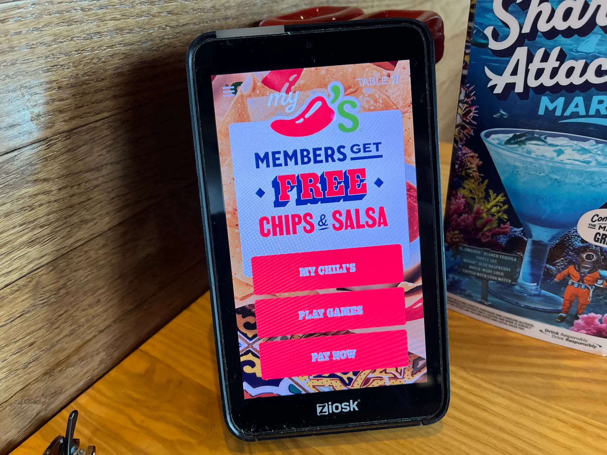 Restaurant table tablet displays a Chili's membership offer for free chips and salsa beside a drink menu.