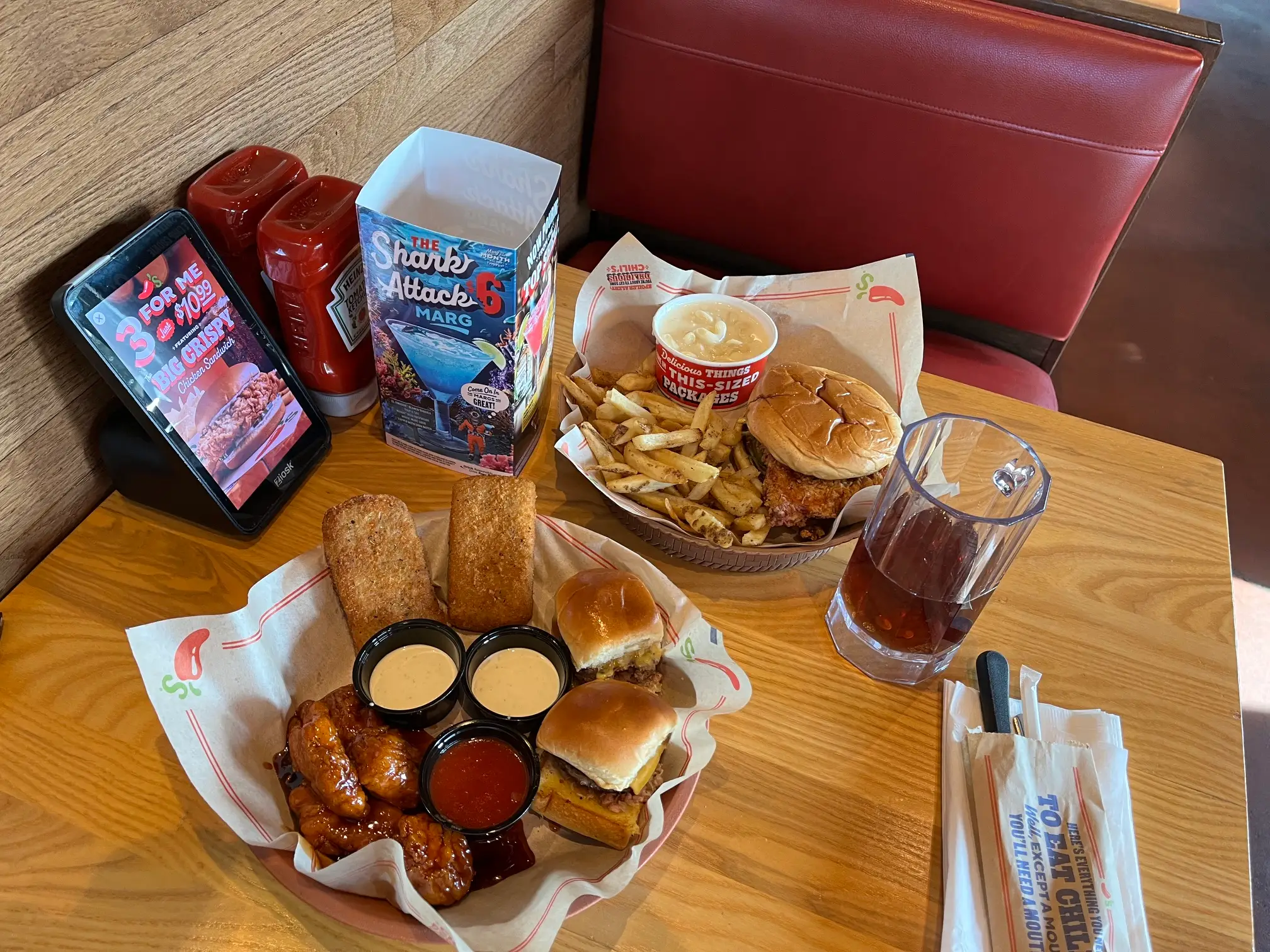 Chili's restaurant booth table with baskets of burgers, fries, wings, sauces, drinks, and tabletop promotional signs.