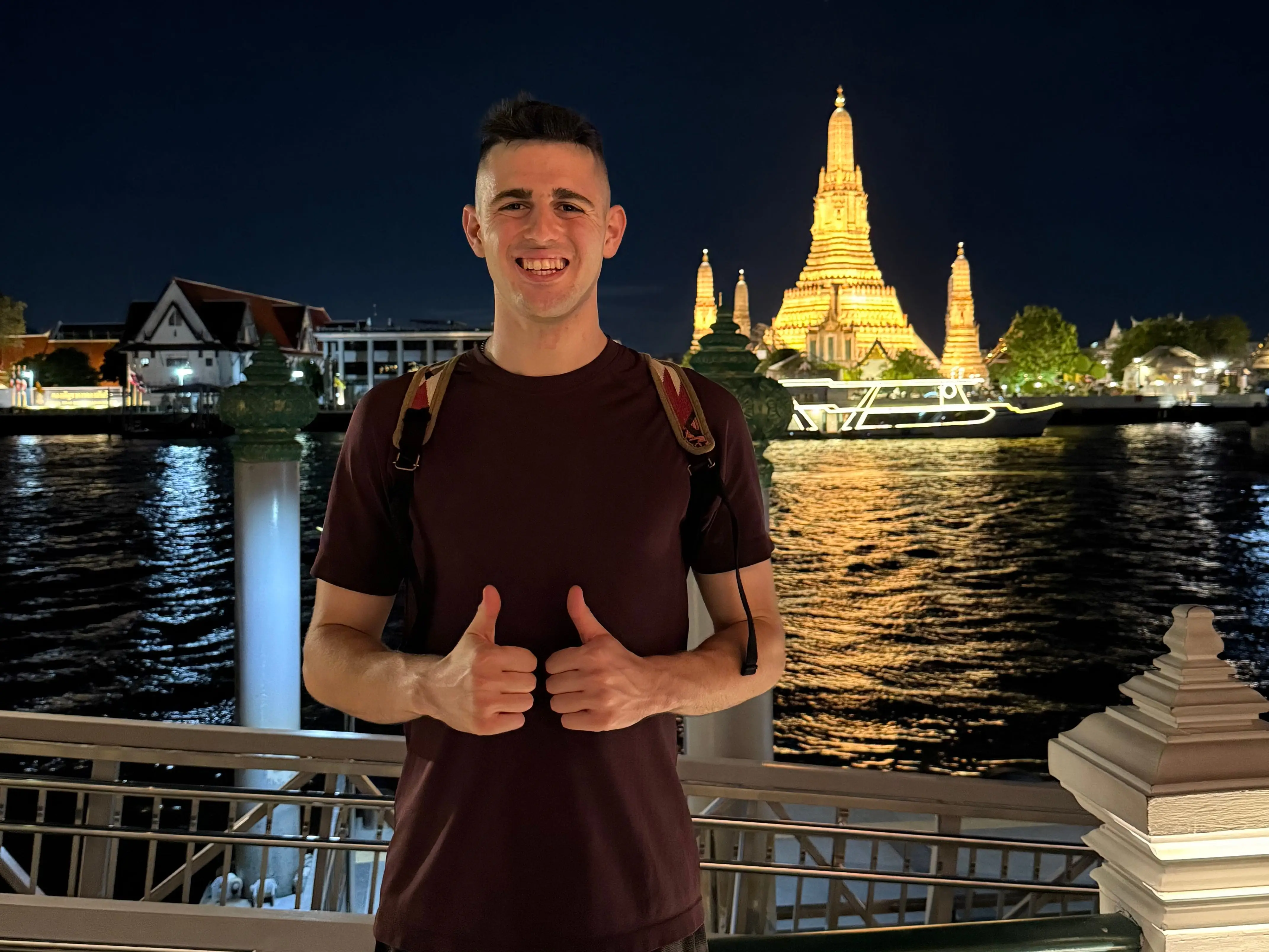 Man giving two thumbs up in front of temple in Thailand at night