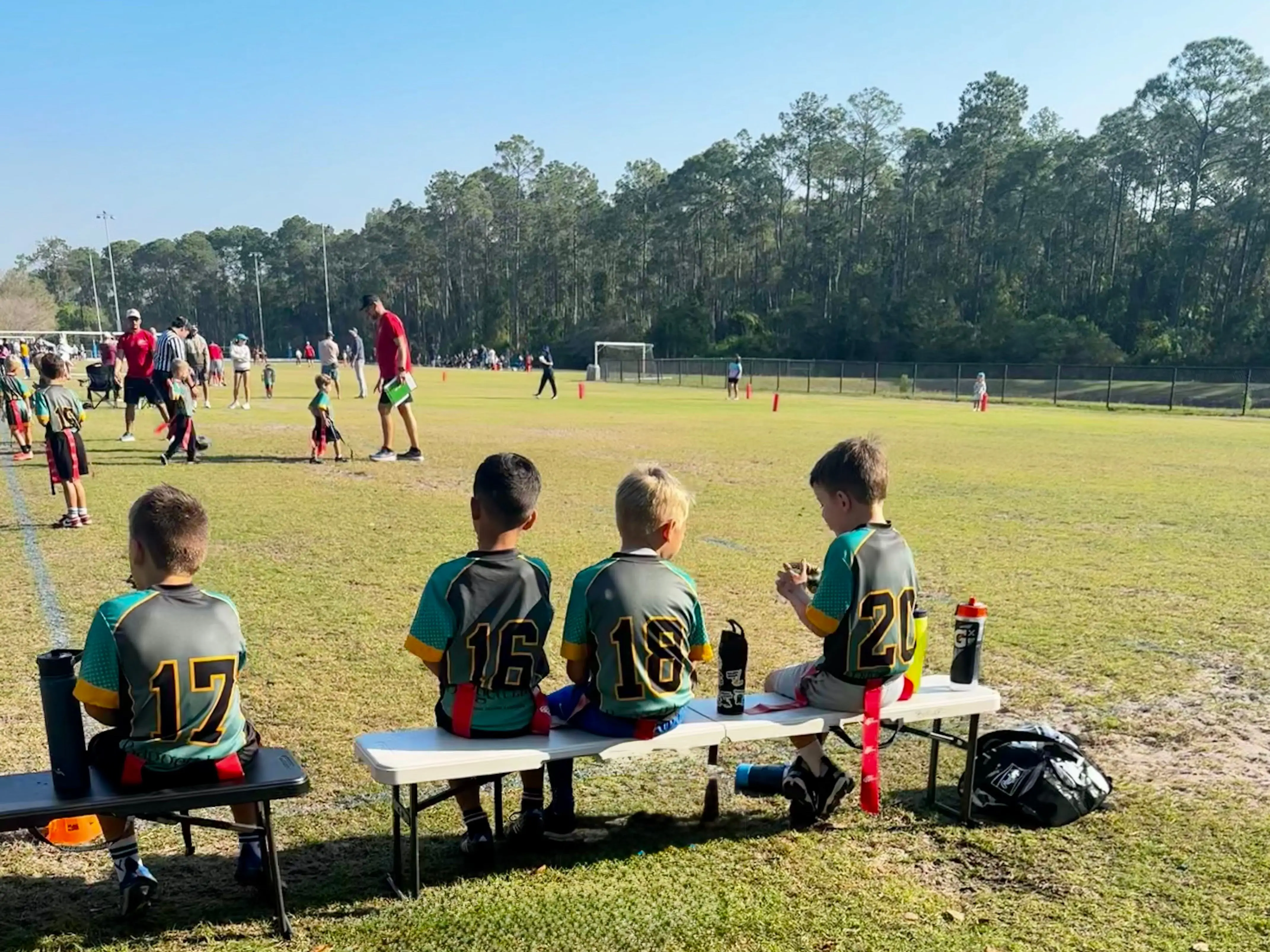 Young boys sit on a bench on the sidelines at a soccer game.