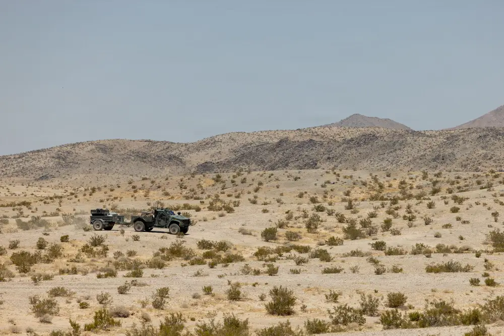A truck carries a trailer in the desert. Inside the trailer is an uncrewed ground vehicle.