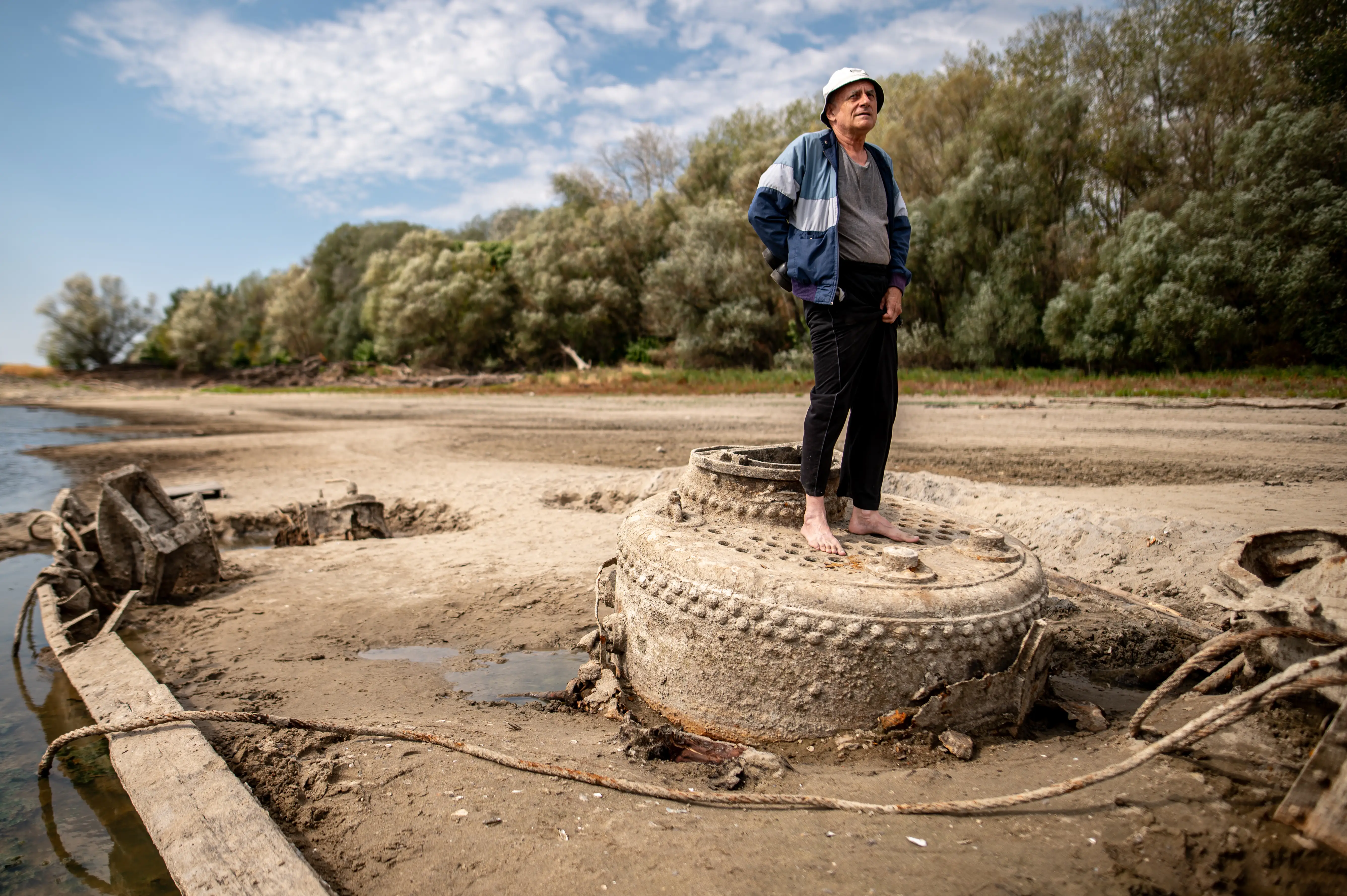 A man stands on top of an old war ship stranded on a dry riverbed.