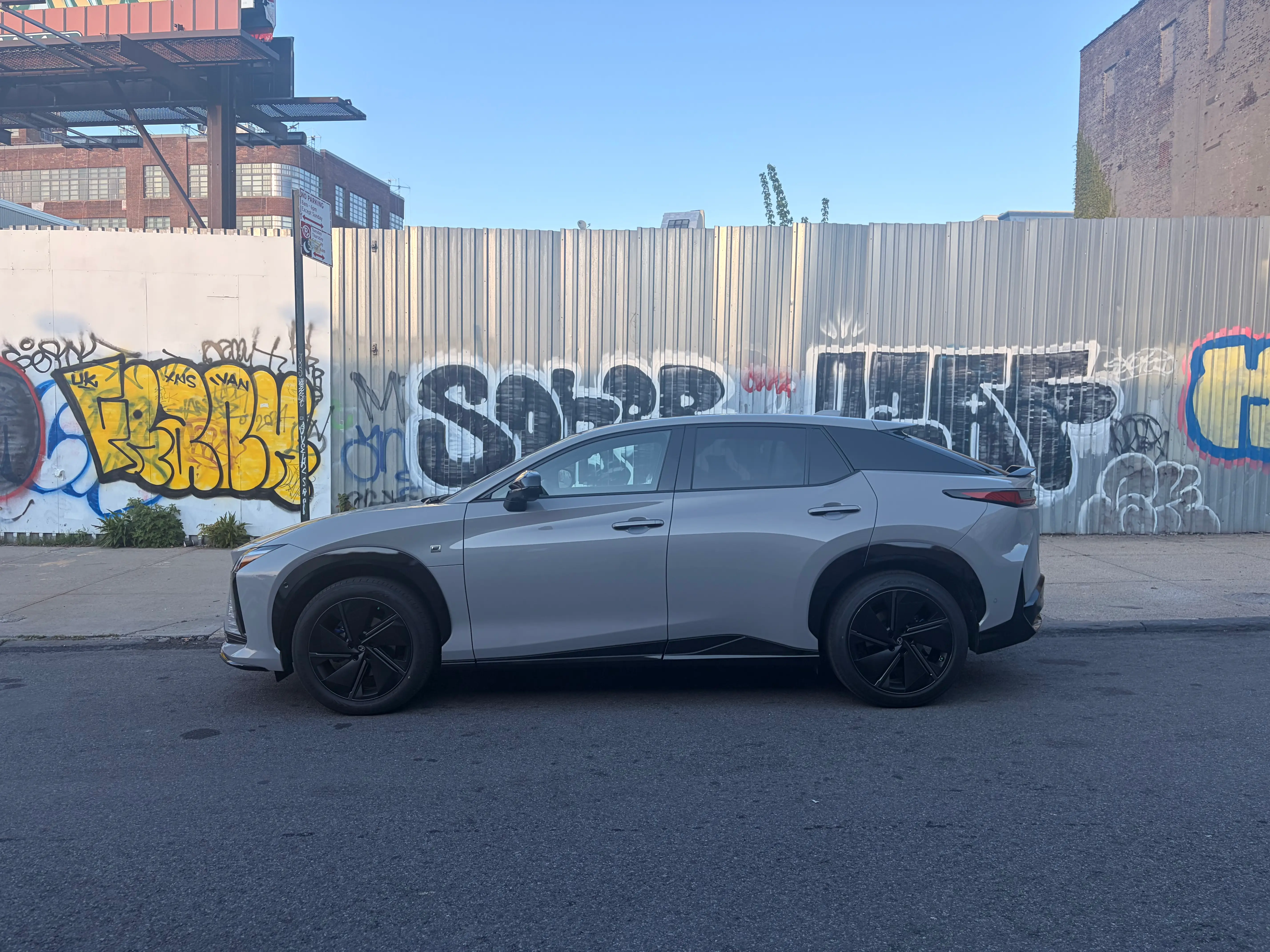 A 2026 Lexus RZ, the bZ's luxury sibling, is parked in front of a graffiti wall.