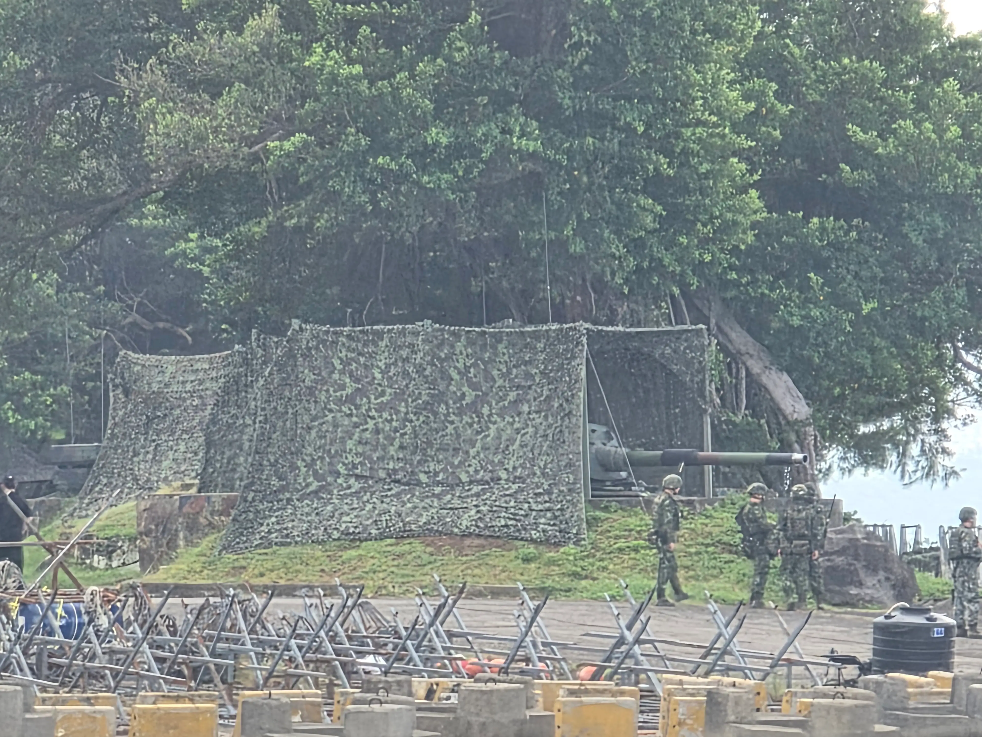 An across-the-river shot of a CM-11 tank shrouded in camoflagued netting.