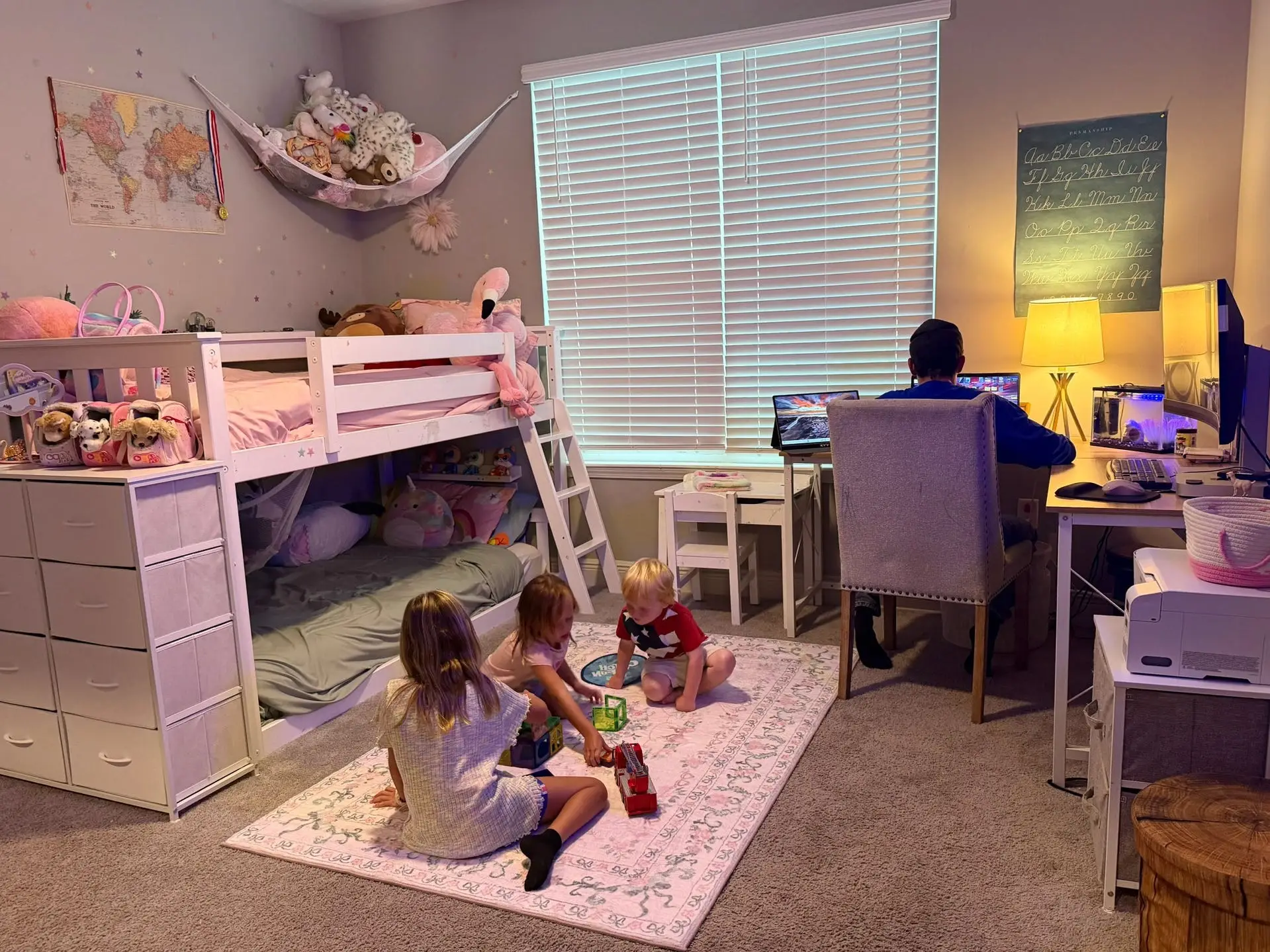 The writer's three children play on a rug while their father sits at a desk in a bedroom with a bunk bed.