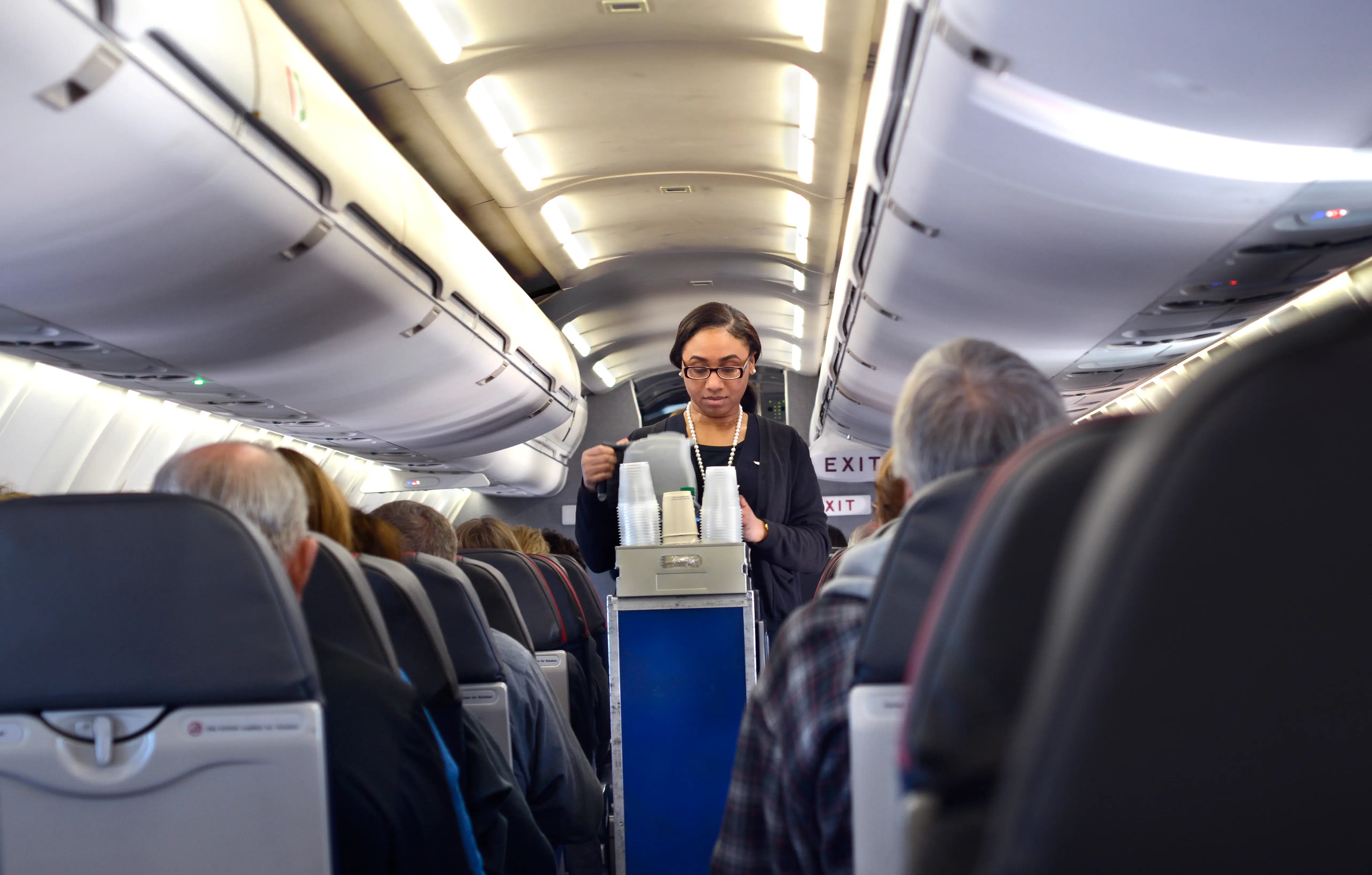 An American Airlines flight attendant walks through a plane's cabin with a drinks cart.