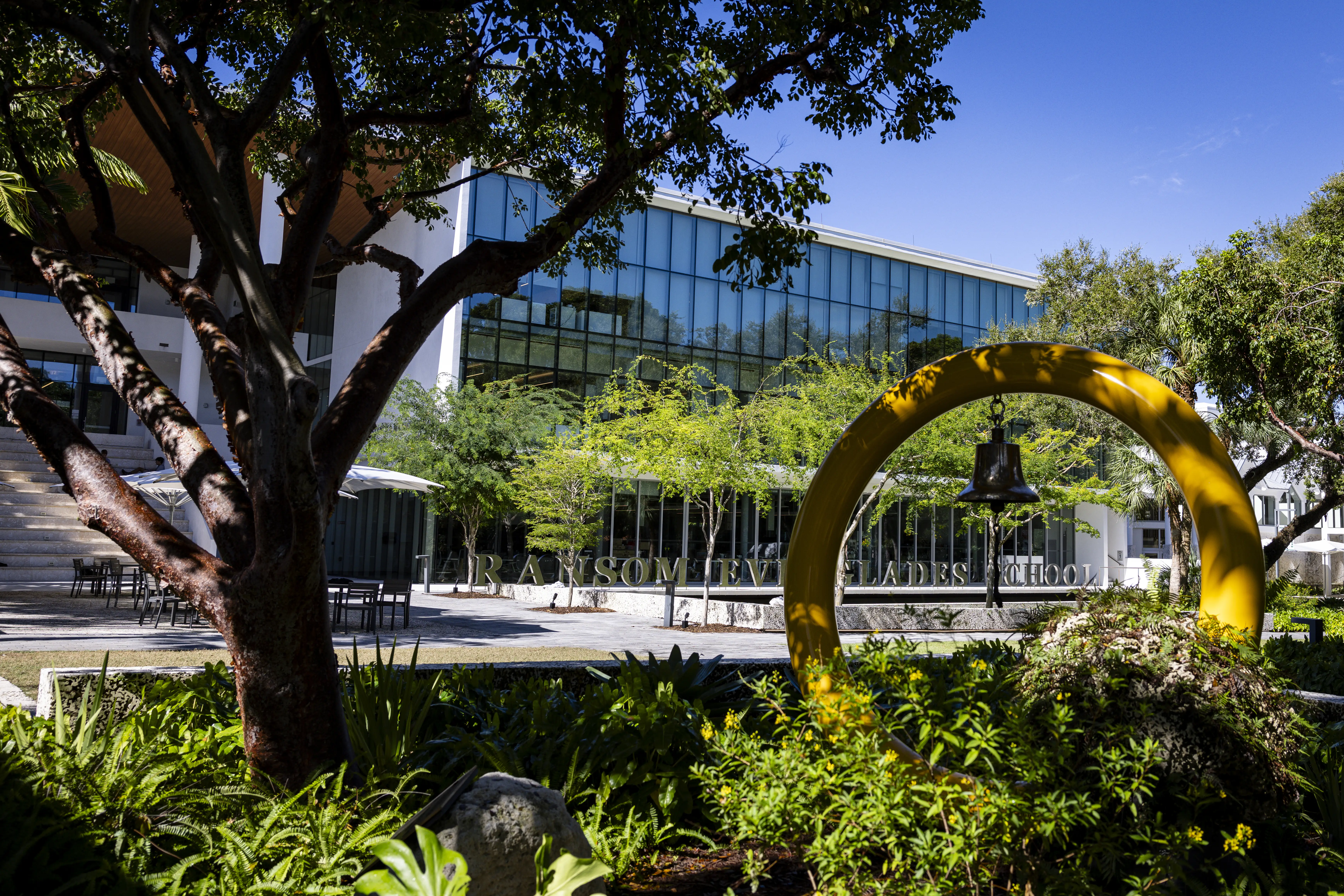 Glass-fronted Ransom Everglades building behind a landscaped garden with a yellow arch and hanging bell.