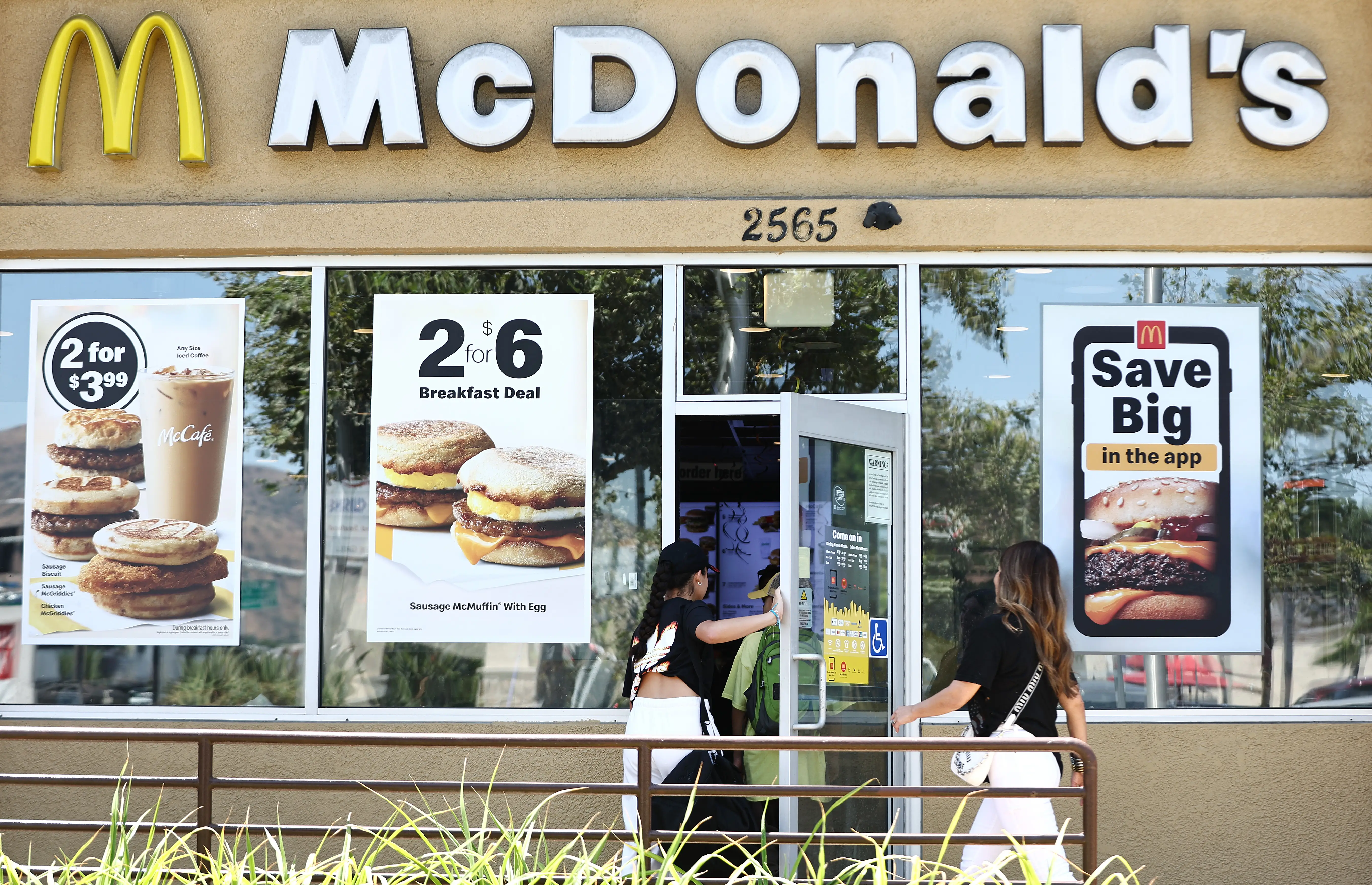 Customers enter a McDonald's restaurant with window posters advertising breakfast deals and app savings.