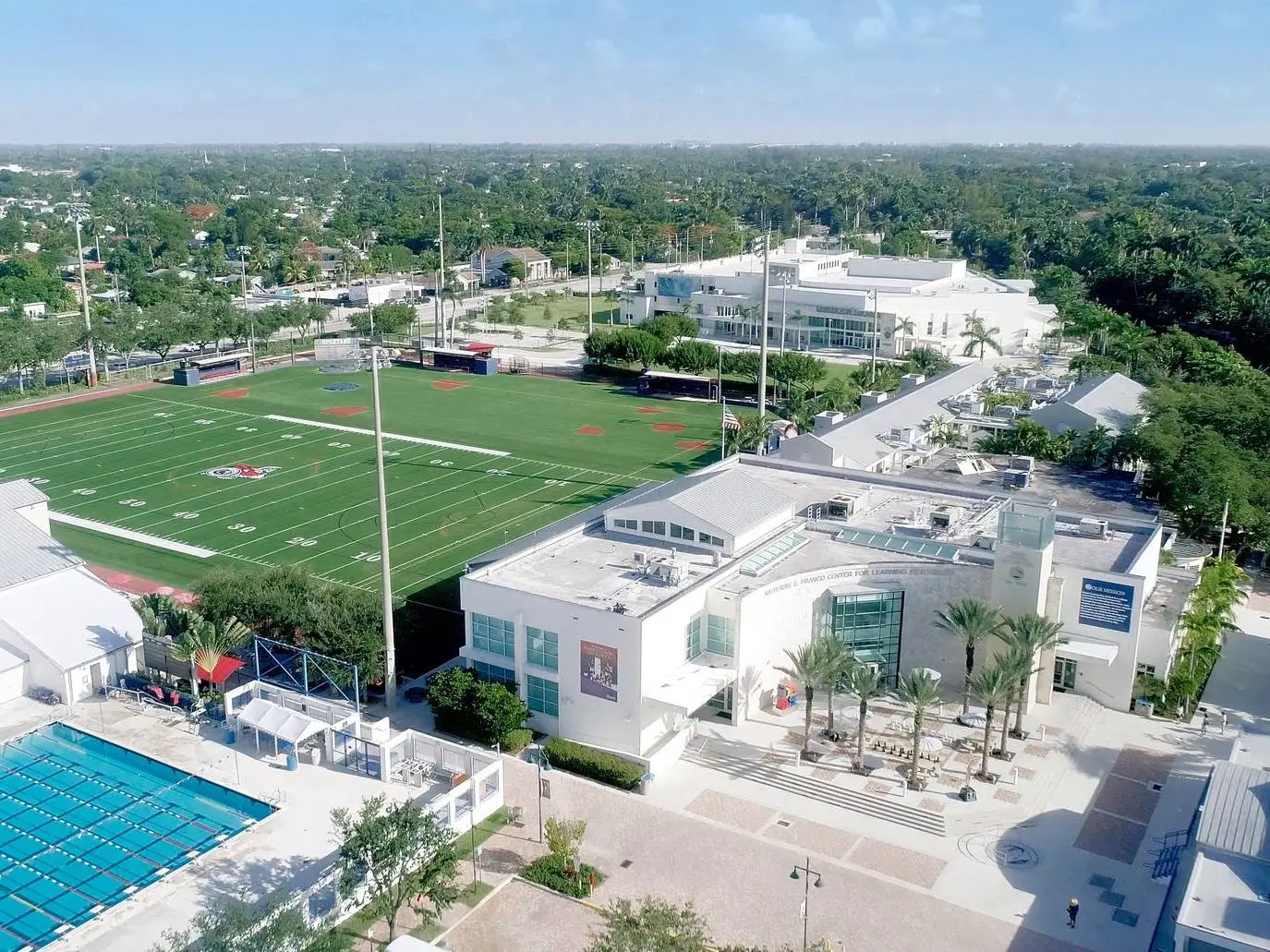 Aerial view of Miami Country Day School with athletic fields, swimming pool, and modern buildings on a sunny day.
