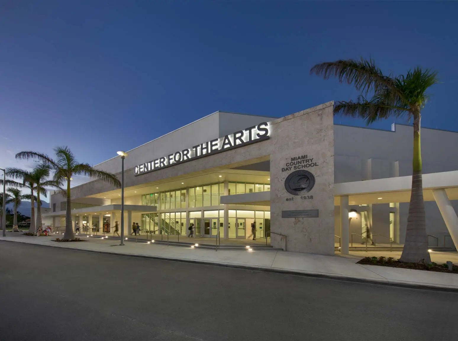Center for the Arts entrance at Miami Country Day School illuminated at dusk with palm trees outside.