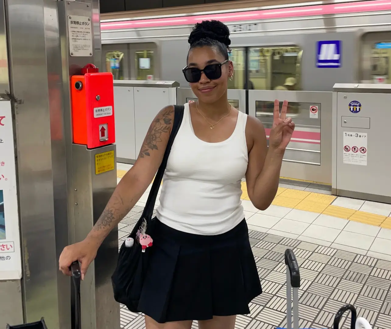 The writer wearing a black skirt and white tank top, standing with suitcases in front of a train.
