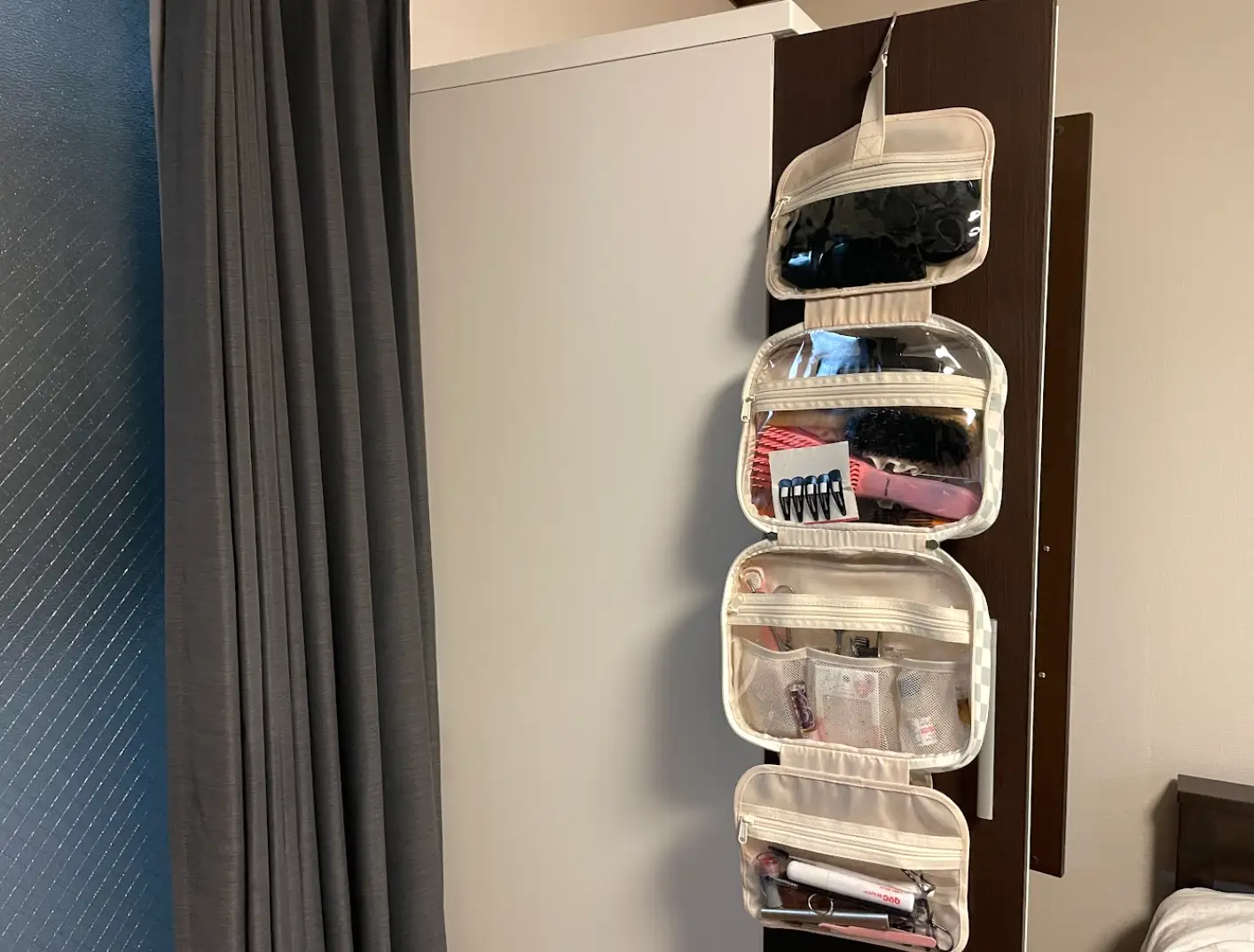 A folding toiletry bag with hair products, makeup items, and more hangs on the writer's dresser.